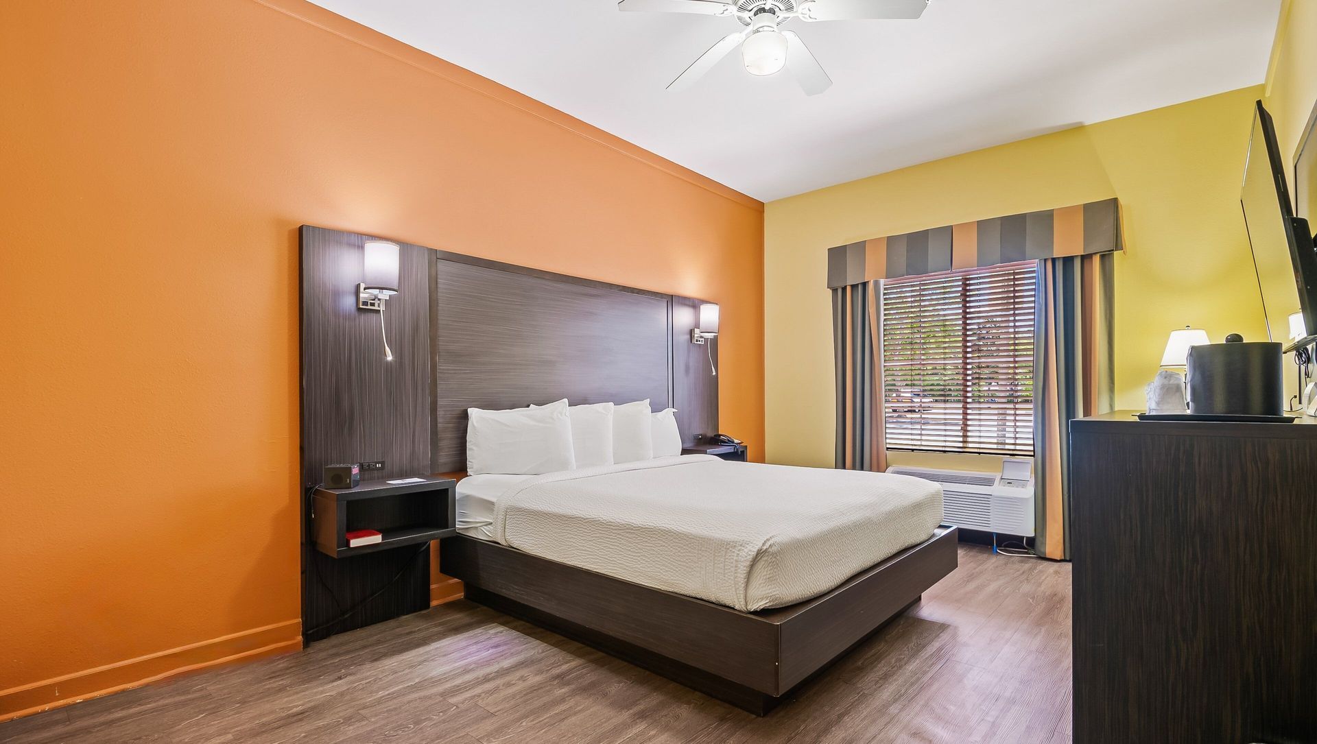 A hotel room with a king size bed and a ceiling fan.