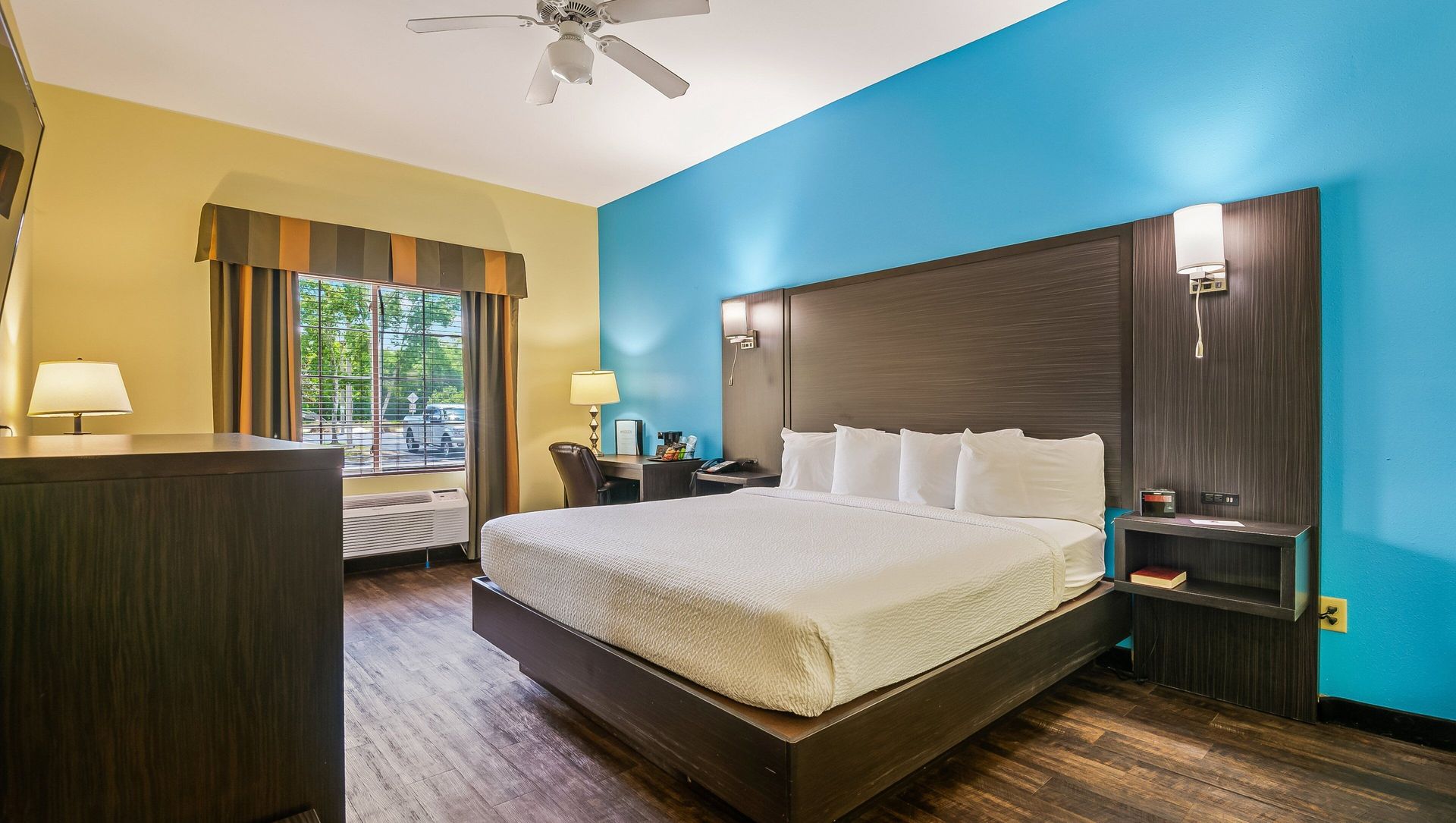 A hotel room with a king size bed and a ceiling fan.