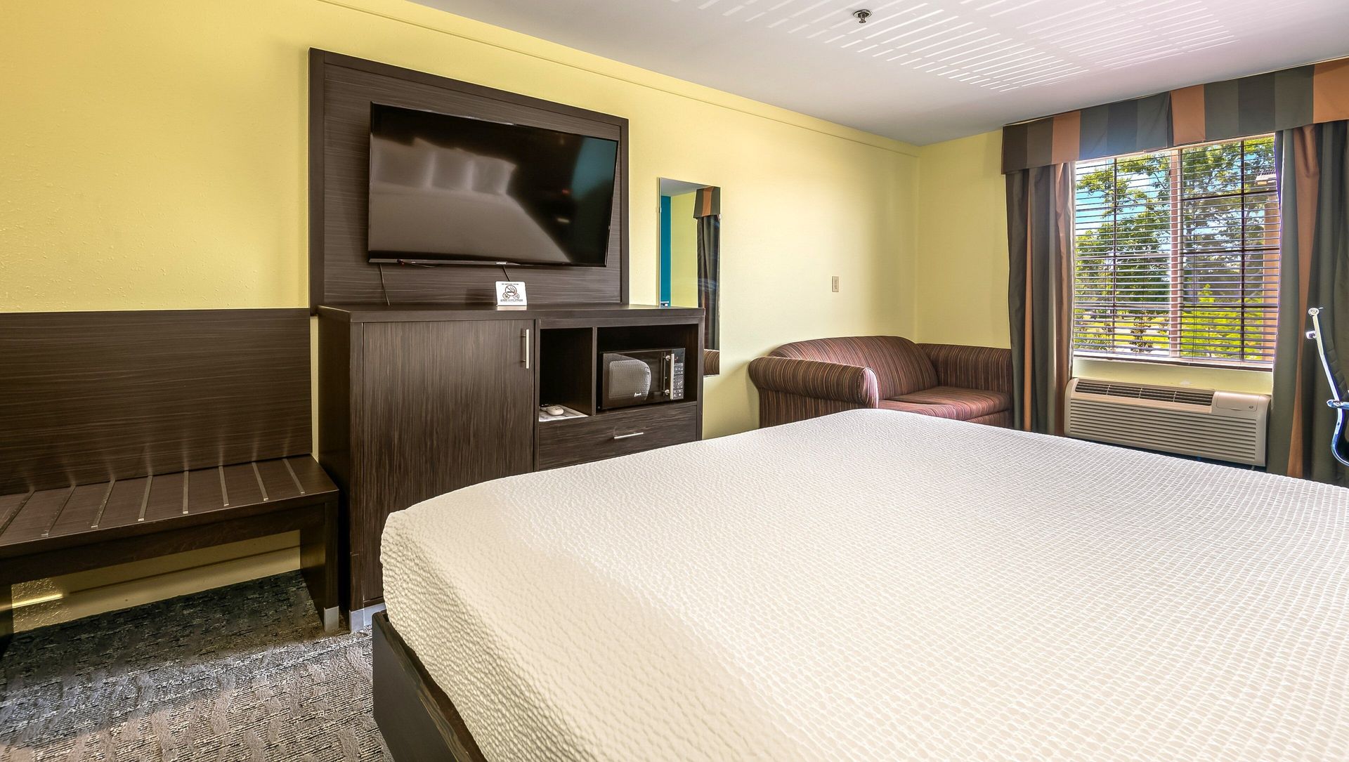 A hotel room with a king size bed , television , chair and sliding glass door.