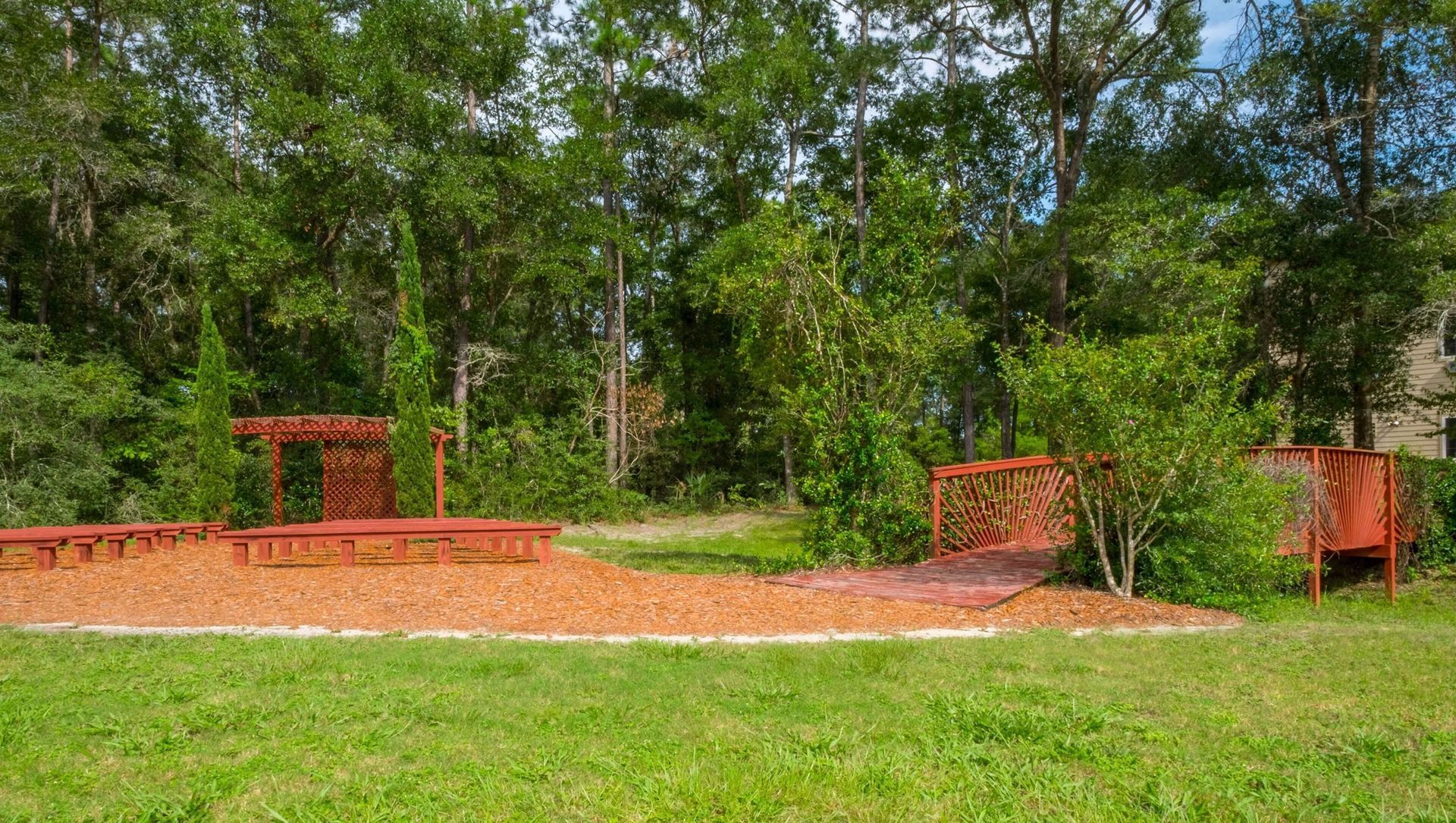 A lush green field with a red bridge in the middle of it surrounded by trees.