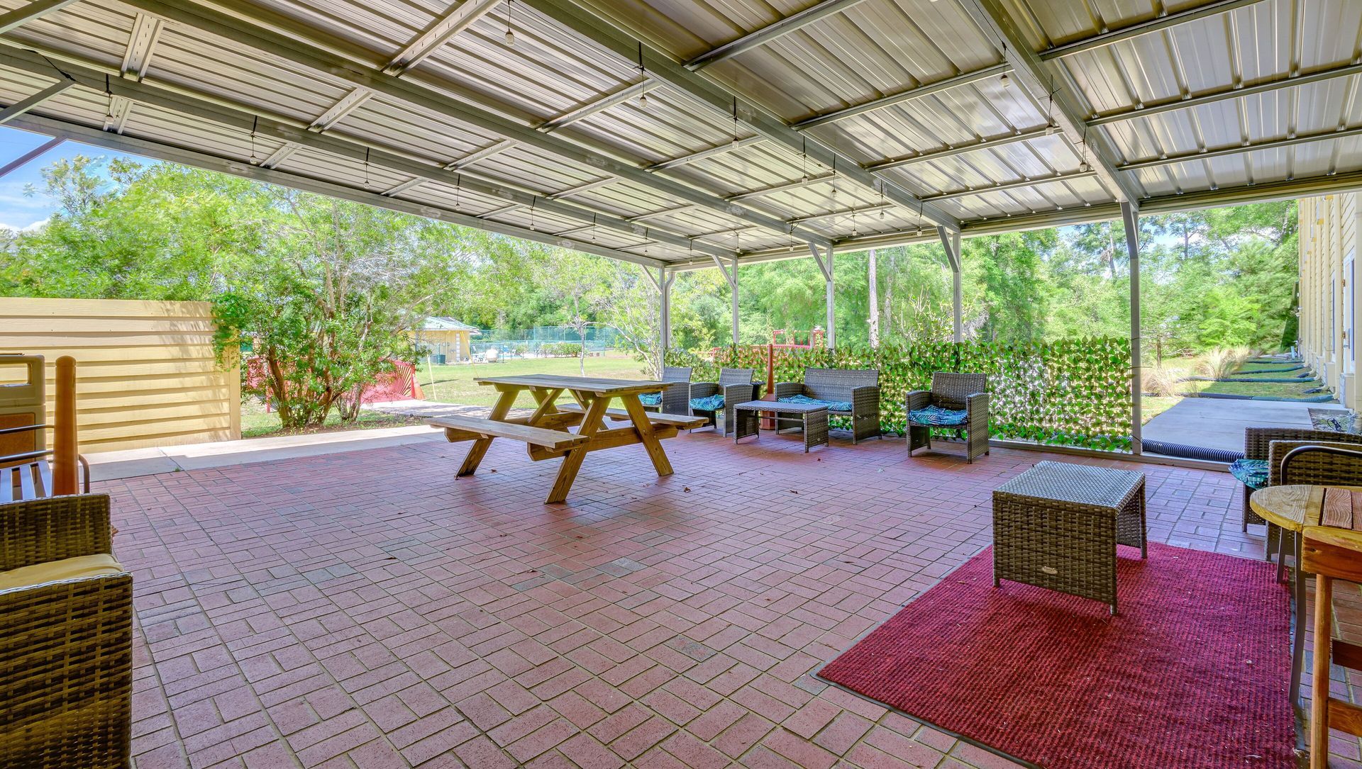 A covered patio with a picnic table and chairs under a roof.