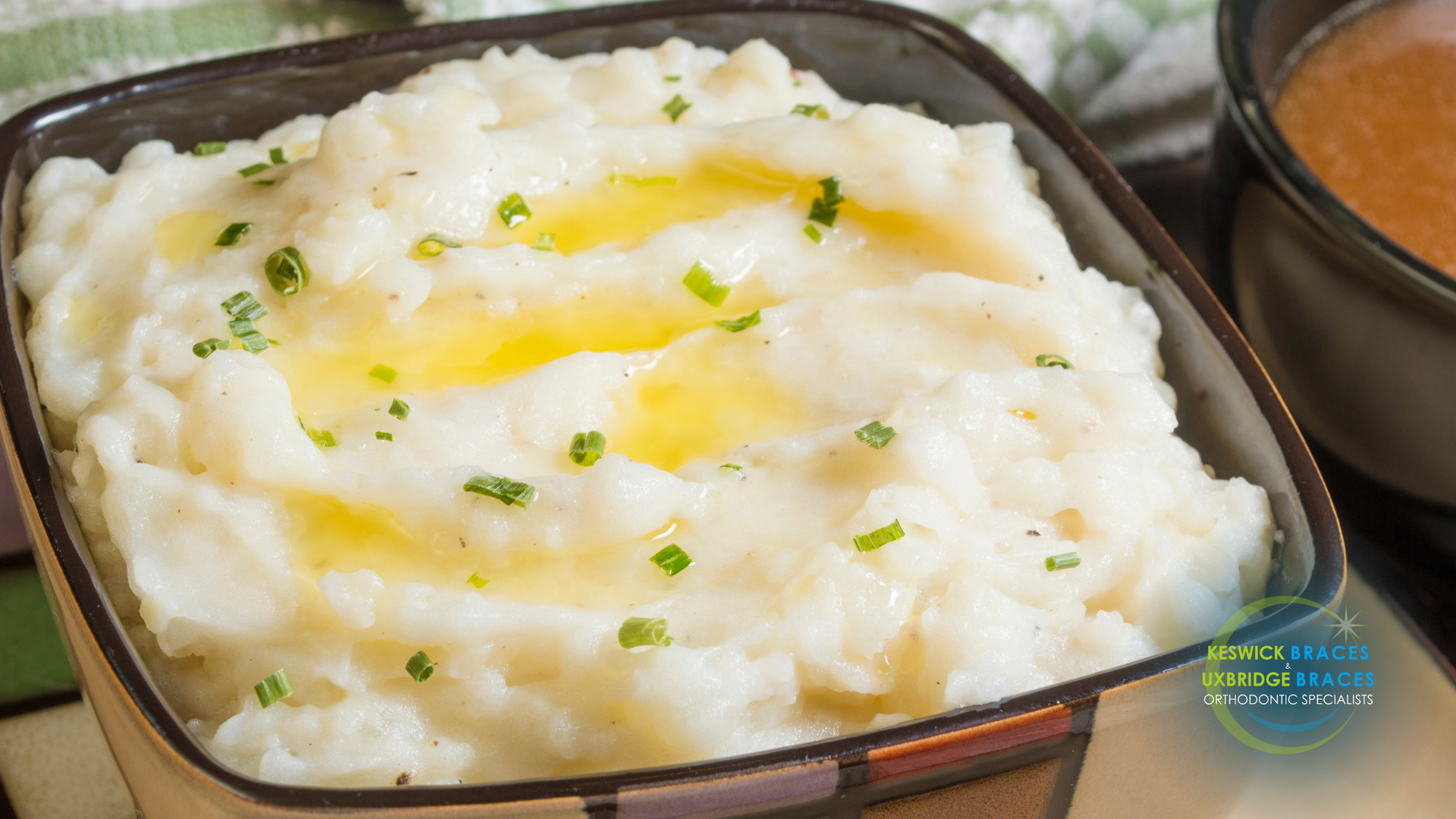 A bowl of mashed potatoes with butter and chives on top.