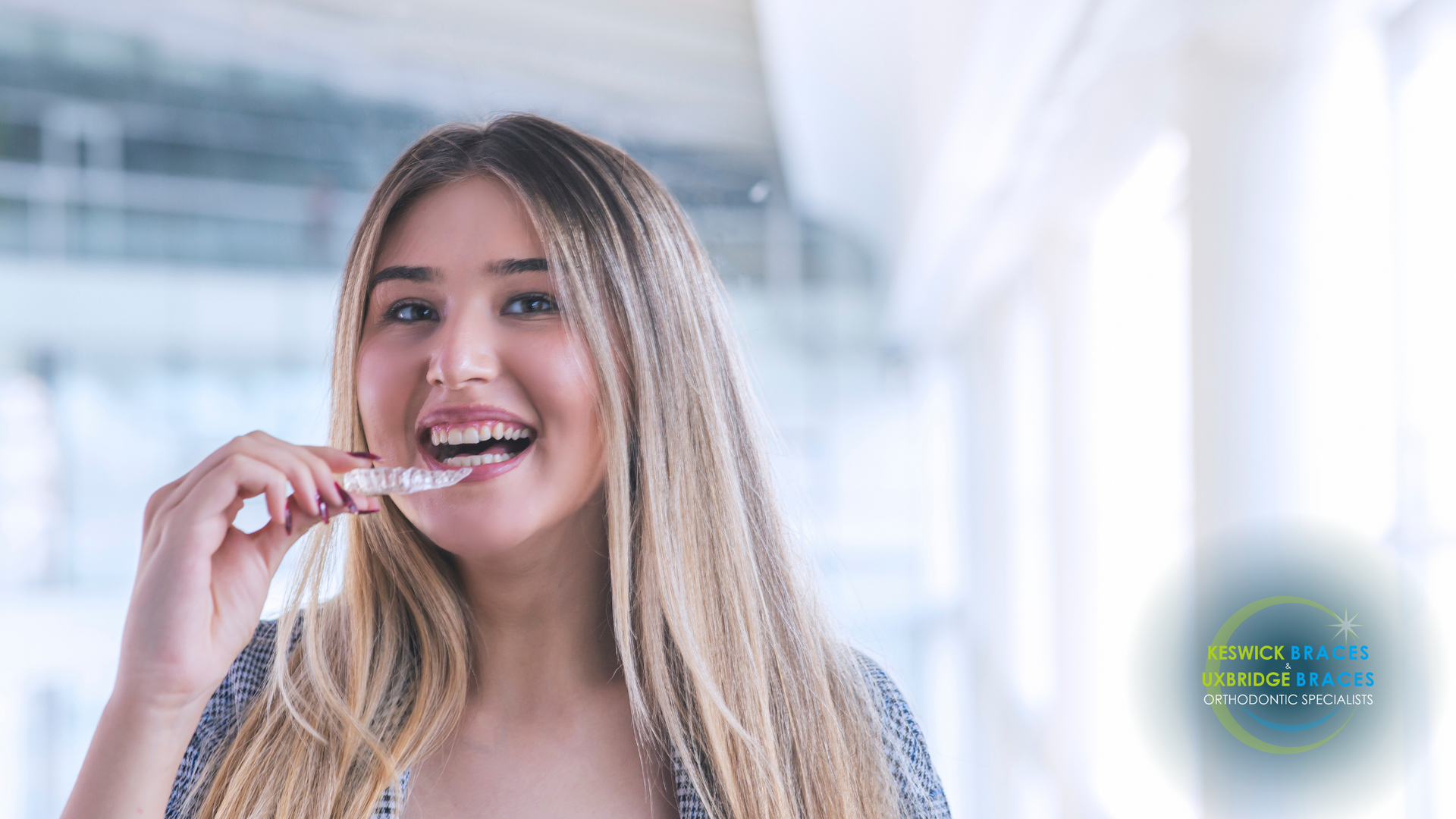 A woman is smiling while holding a clear brace in her mouth.