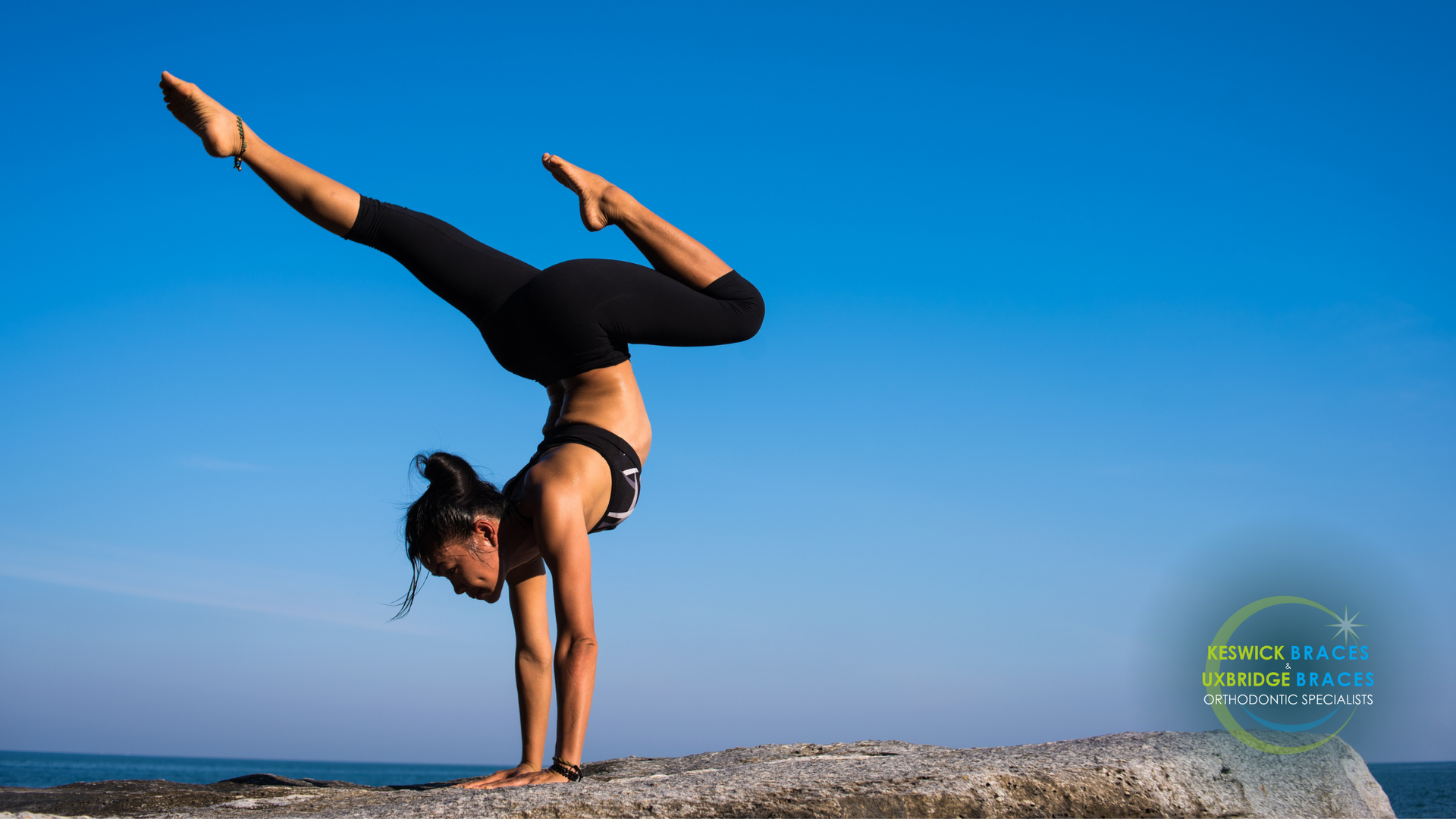 A woman is doing a handstand on a rock near the ocean.