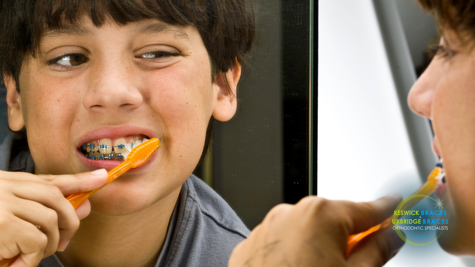 A boy with braces is brushing his teeth in front of a mirror