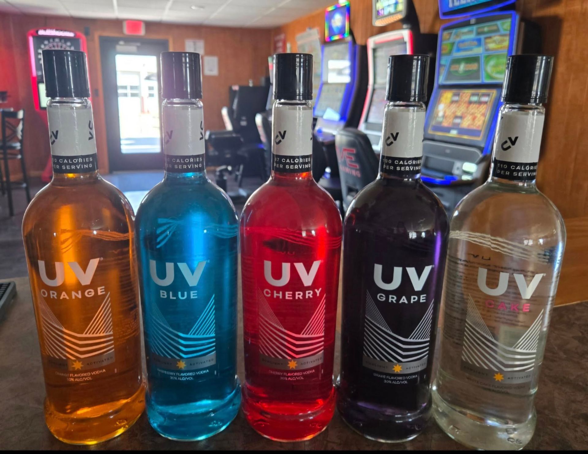 Five bottles of UV vodka, orange, blue, cherry, grape, and original, displayed on a bar.