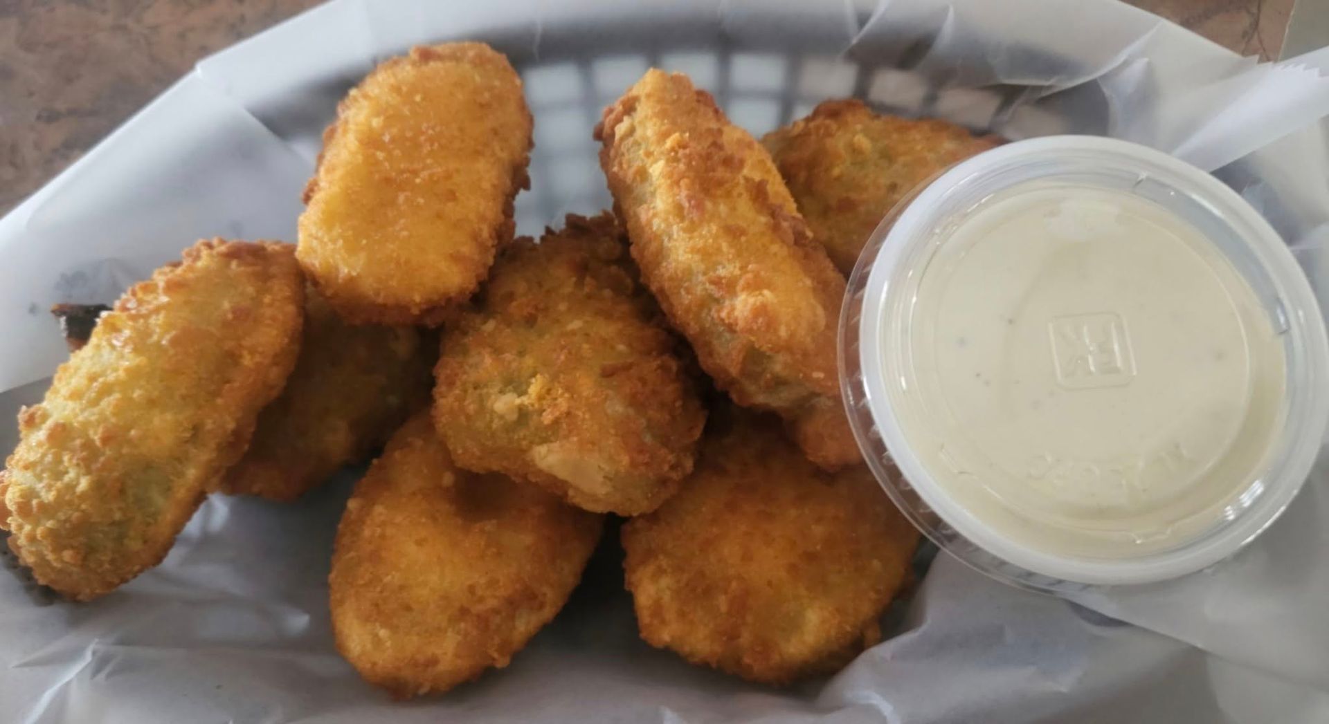 Basket of fried jalapeño poppers with a side of creamy dipping sauce.