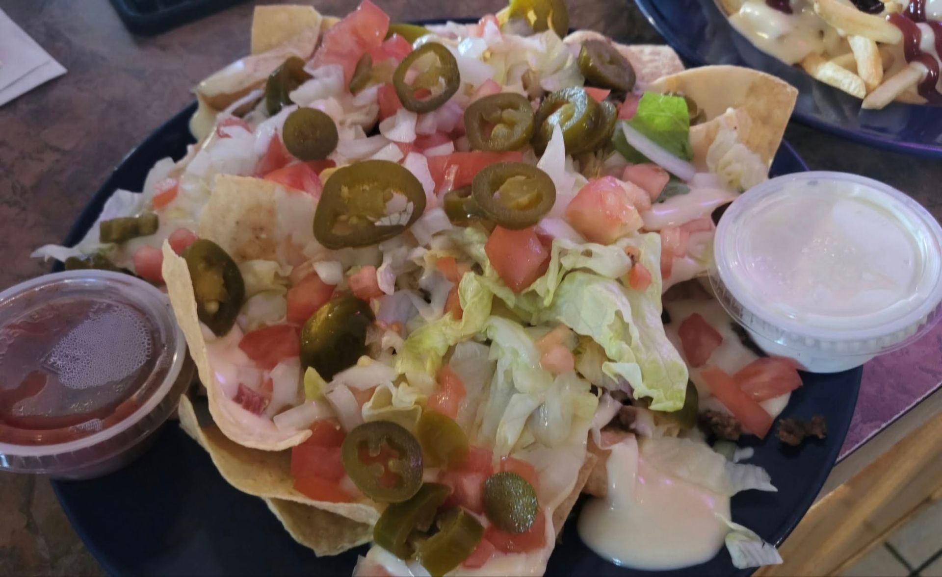 Nachos on a blue plate with salsa, sour cream, and toppings: jalapeños, tomatoes, and lettuce.