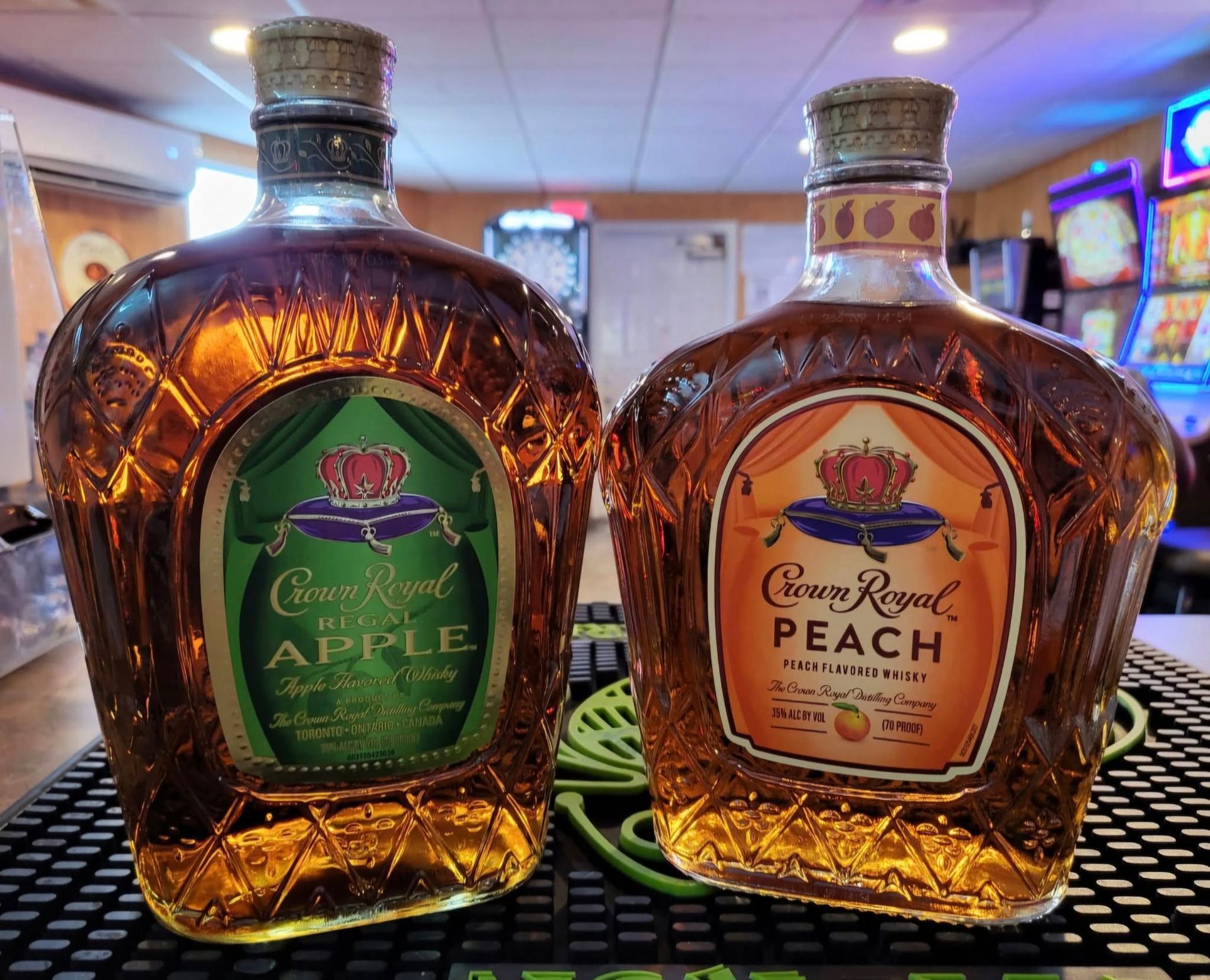 Two Crown Royal liquor bottles, Apple and Peach flavors, on a bar counter.