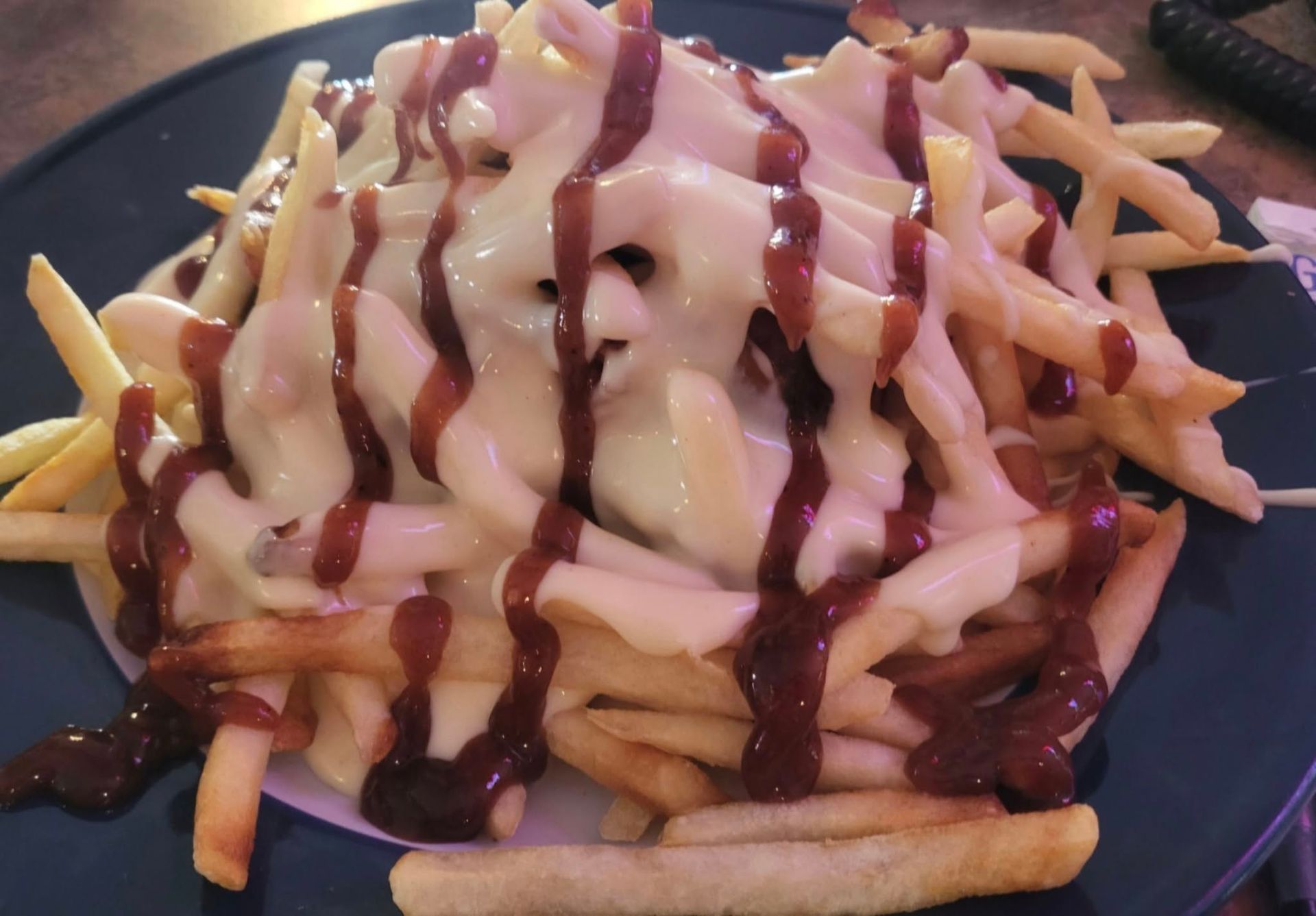 Fries topped with white cheese sauce and drizzled with a dark brown sauce on a blue plate.