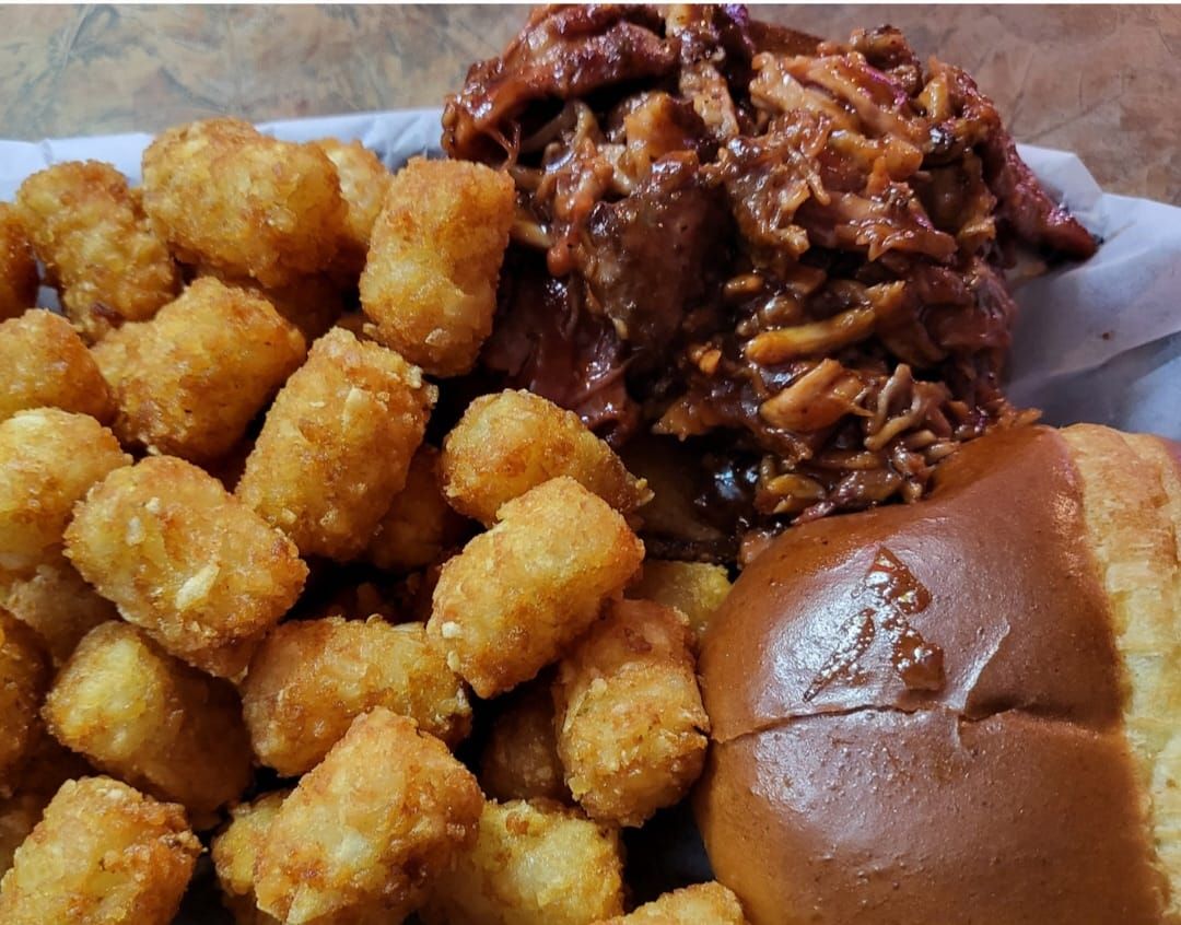Pulled pork sandwich with tater tots and a roll on a tray.