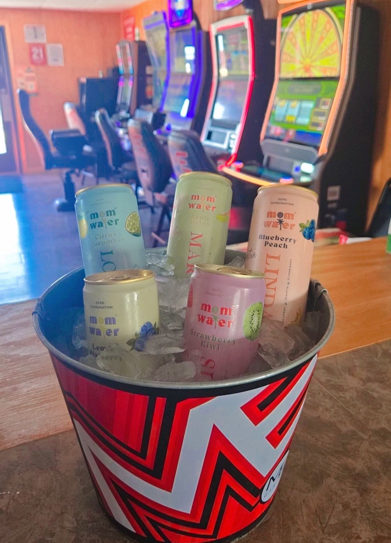 Bucket of canned alcoholic drinks on ice in a bar, with slot machines in the background.
