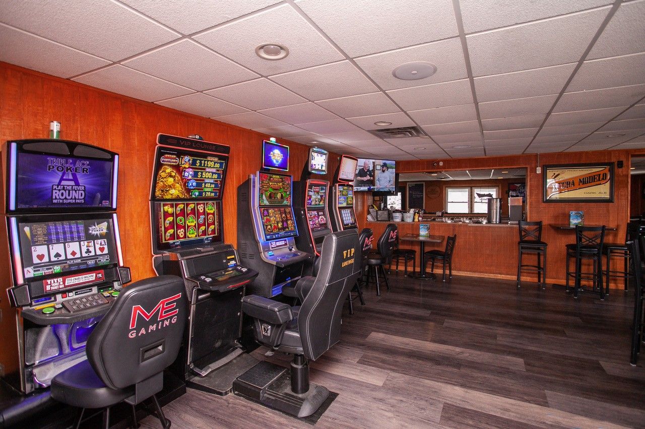 A dimly lit room with slot machines, a bar, and seating.