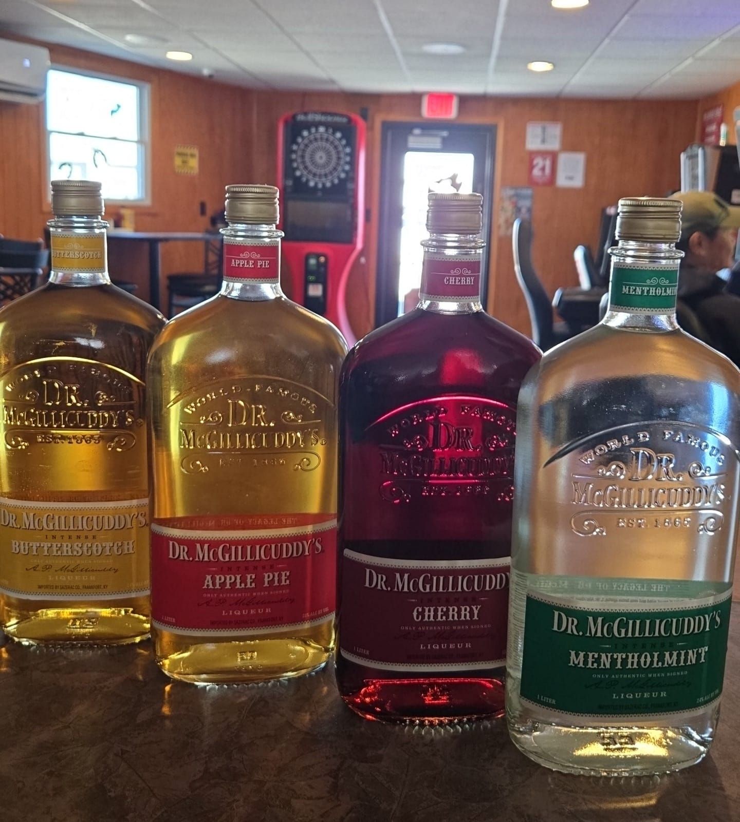 Four bottles of Dr. McGillicuddy's liquor on a bar: apple pie, cherry, peppermint, and original.