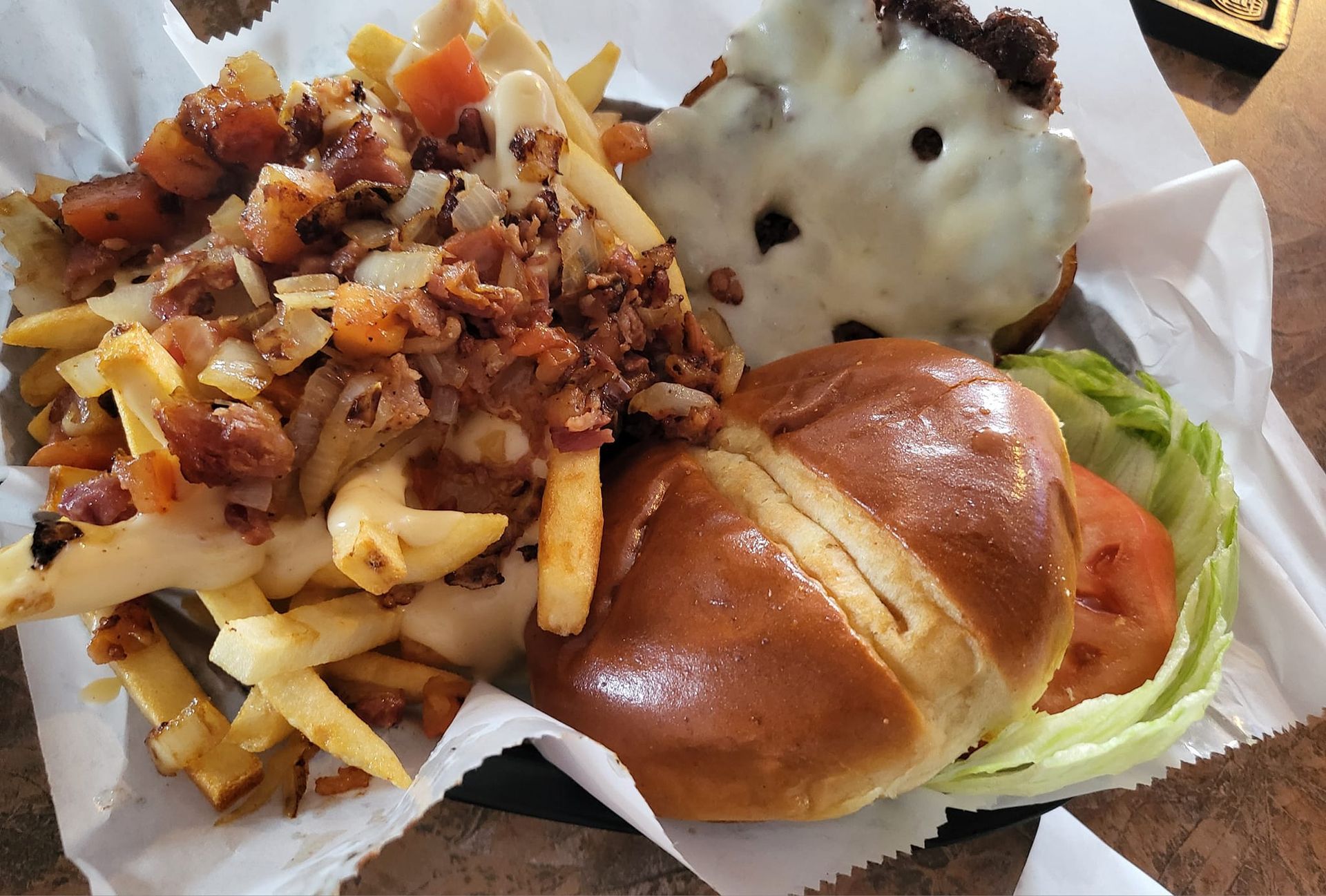 Fries topped with meat and onions, burger with cheese, tomato, and lettuce on a pretzel bun.