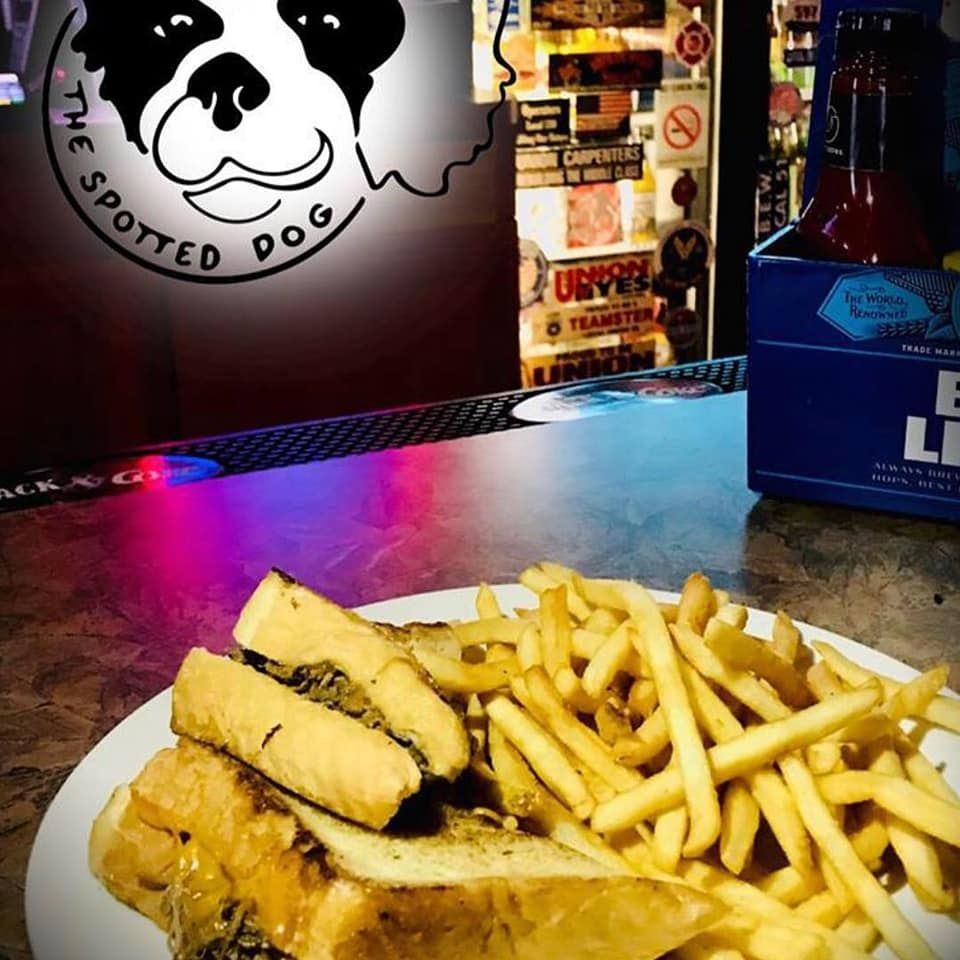 A sandwich and fries on a plate at The Spotted Dog bar, with a beer in the background.