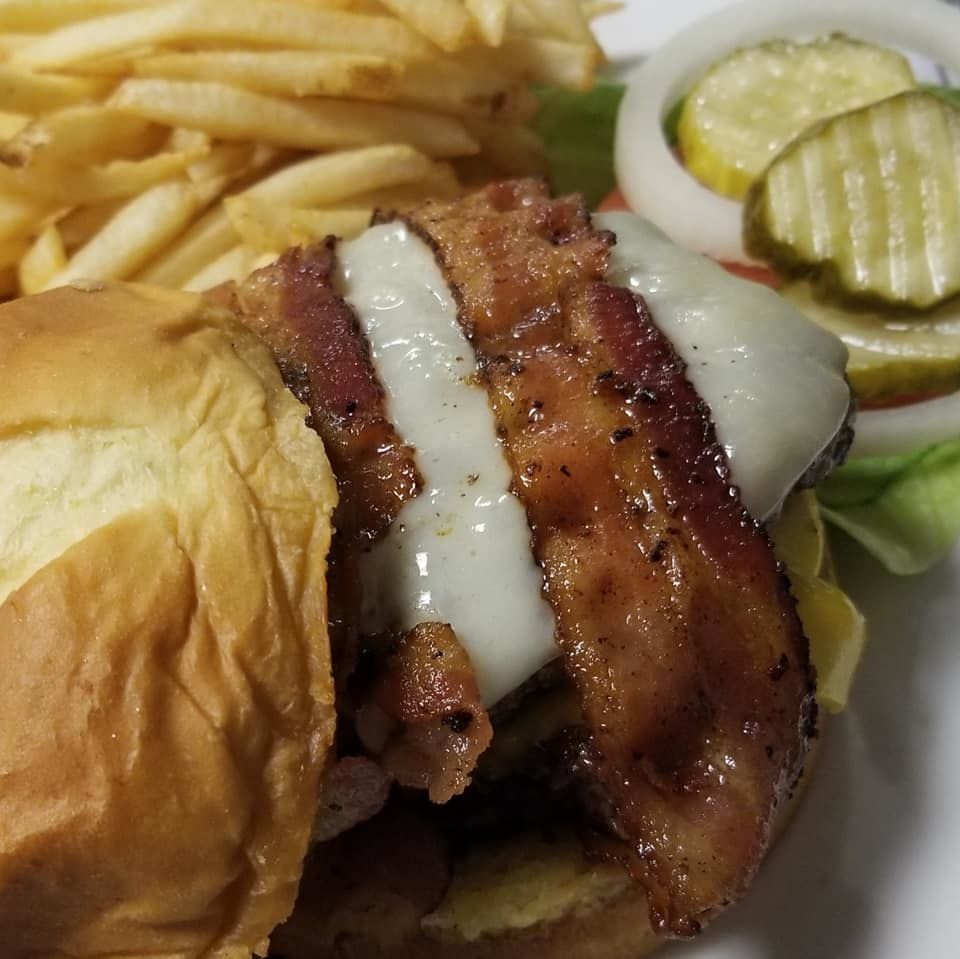 Bacon cheeseburger on a bun with fries, pickles, and onion slices on a plate.