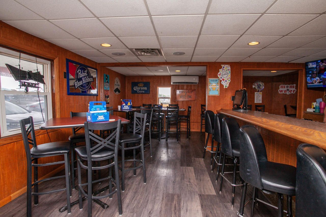 Interior of a bar with tables, chairs, a bar counter, and several beer signs on the wooden panel walls.