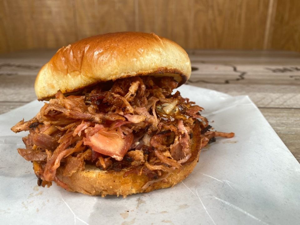 Pulled pork sandwich on a brioche bun, on white paper, wooden background.
