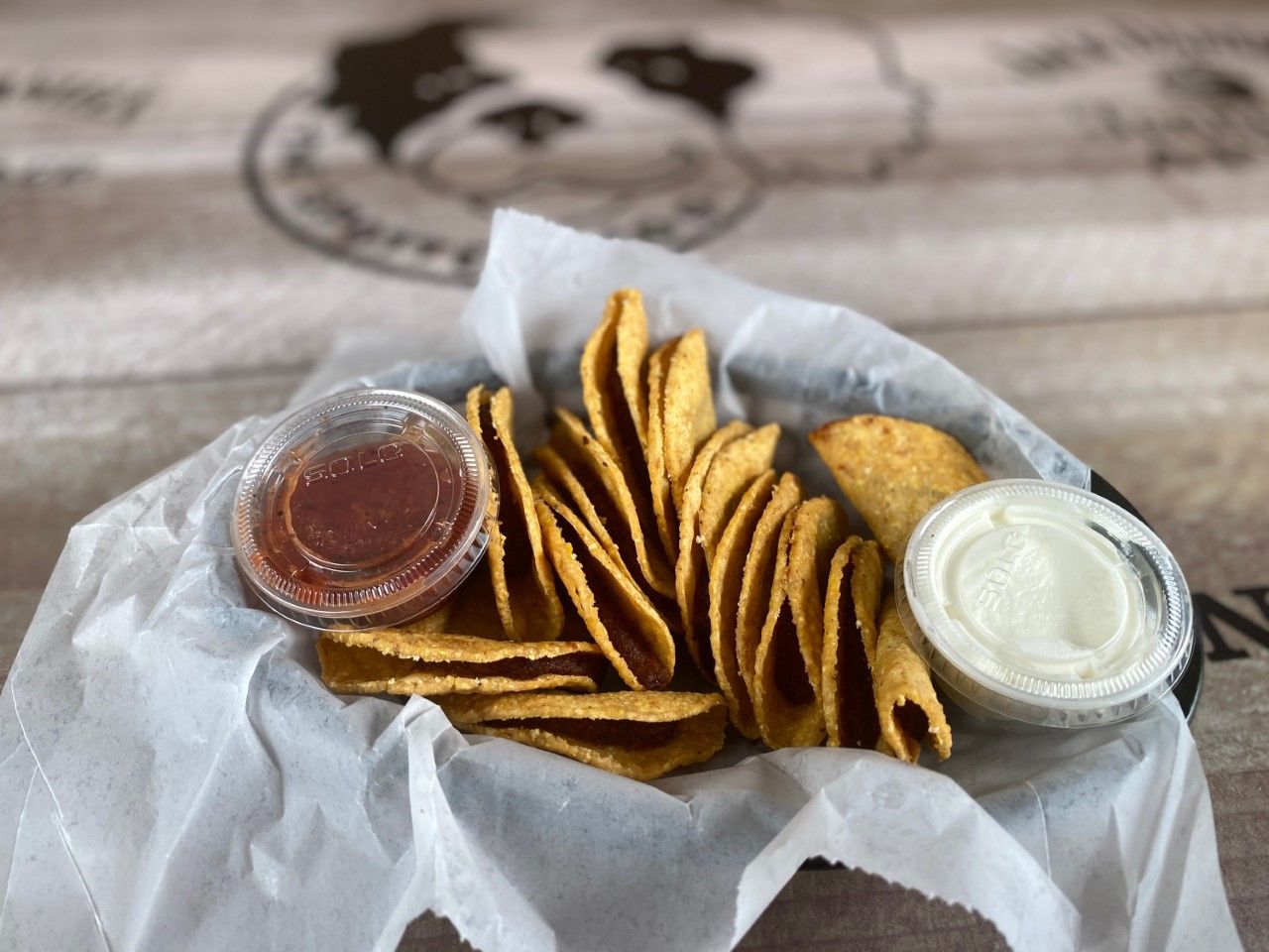Basket of tortilla chips with red sauce and sour cream.