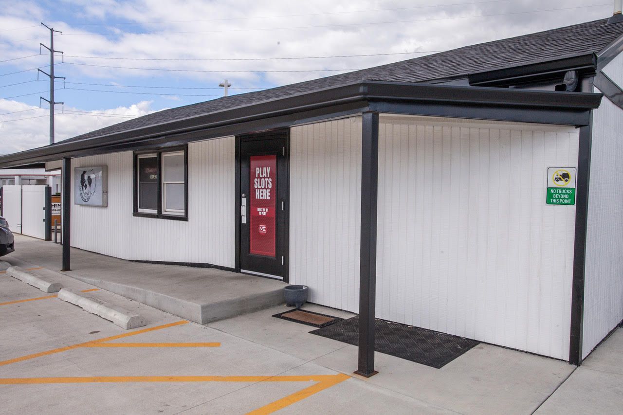 Exterior of a white building with black trim, a red door, and a black awning. Yellow parking lines.