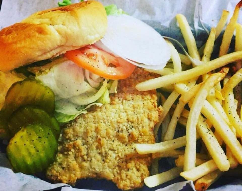 Fried chicken sandwich with fries, pickles, tomato, and onion in a basket.