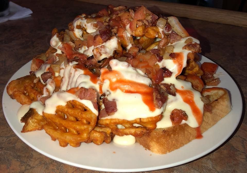 Plate of waffle fries, bacon, and sauce, likely a loaded fries dish.