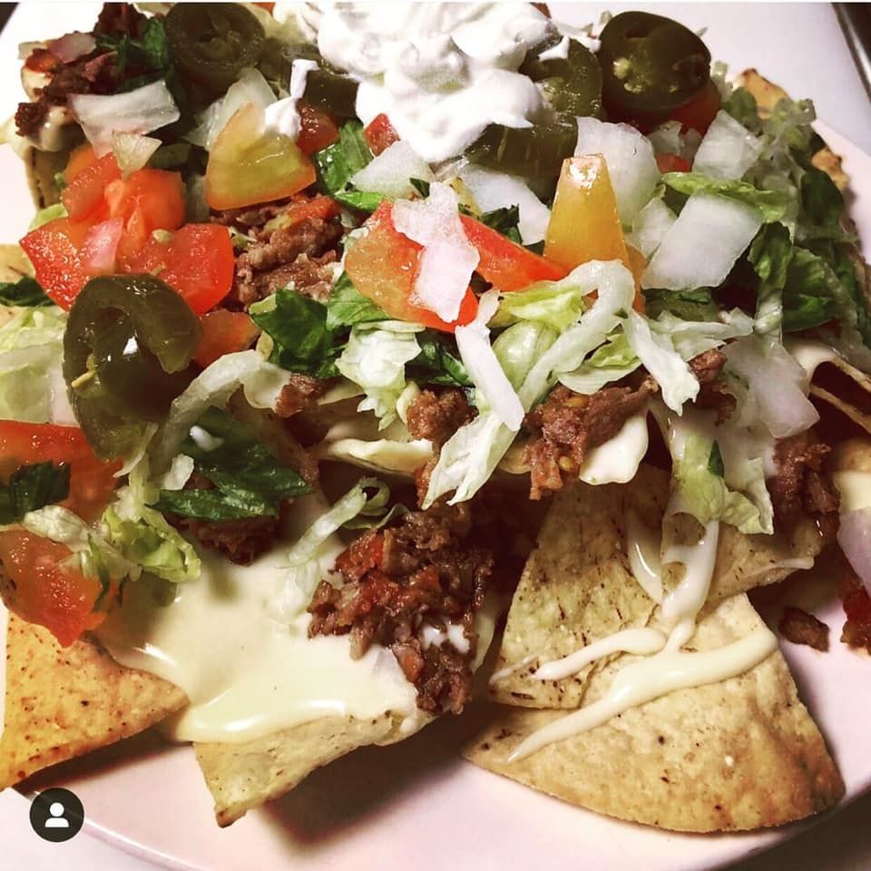 Nachos with meat, cheese, tomatoes, lettuce, jalapeños, and sour cream on a plate.