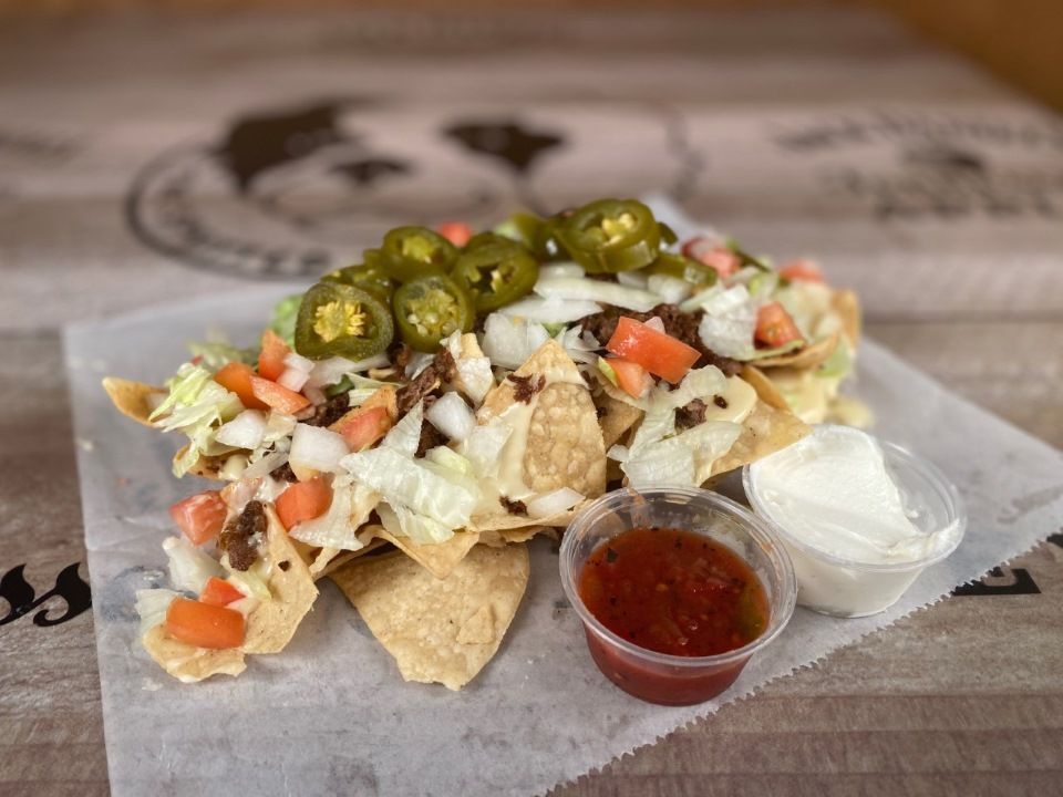 Nachos with toppings of jalapenos, tomatoes, onions, meat, lettuce, and two sides: salsa and sour cream.