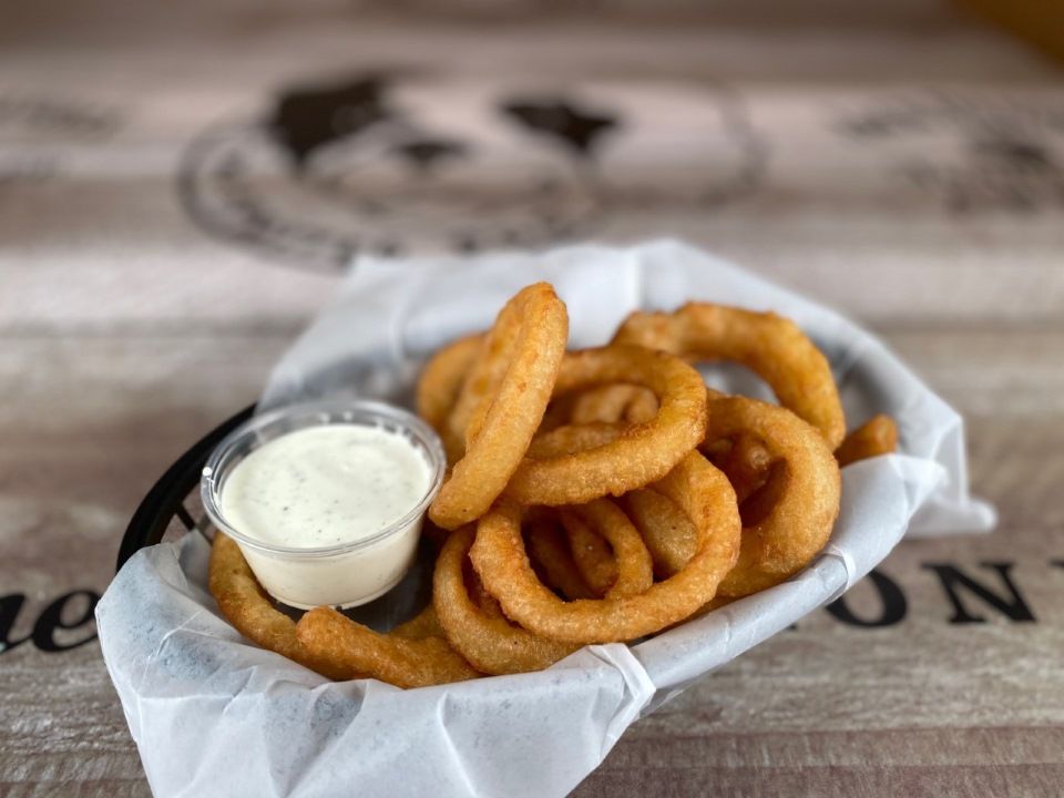 Basket of golden onion rings with a side of white dipping sauce.