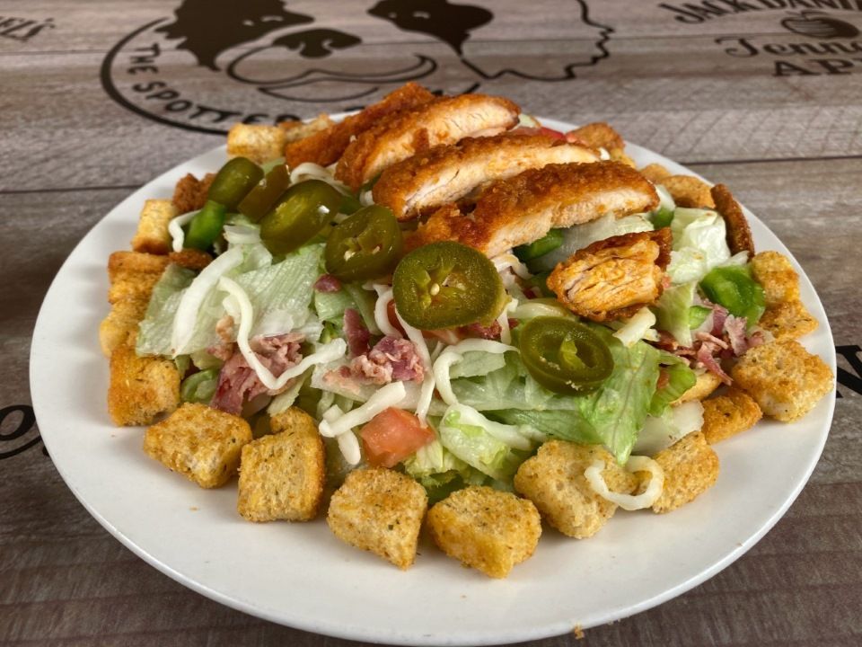 Salad with croutons, lettuce, sliced chicken, jalapenos, and other ingredients on a white plate.