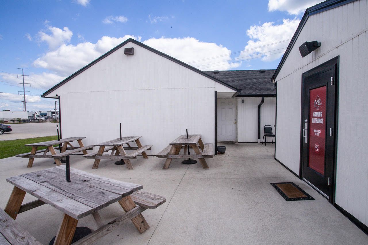 White building exterior with picnic tables on a concrete patio; red door.
