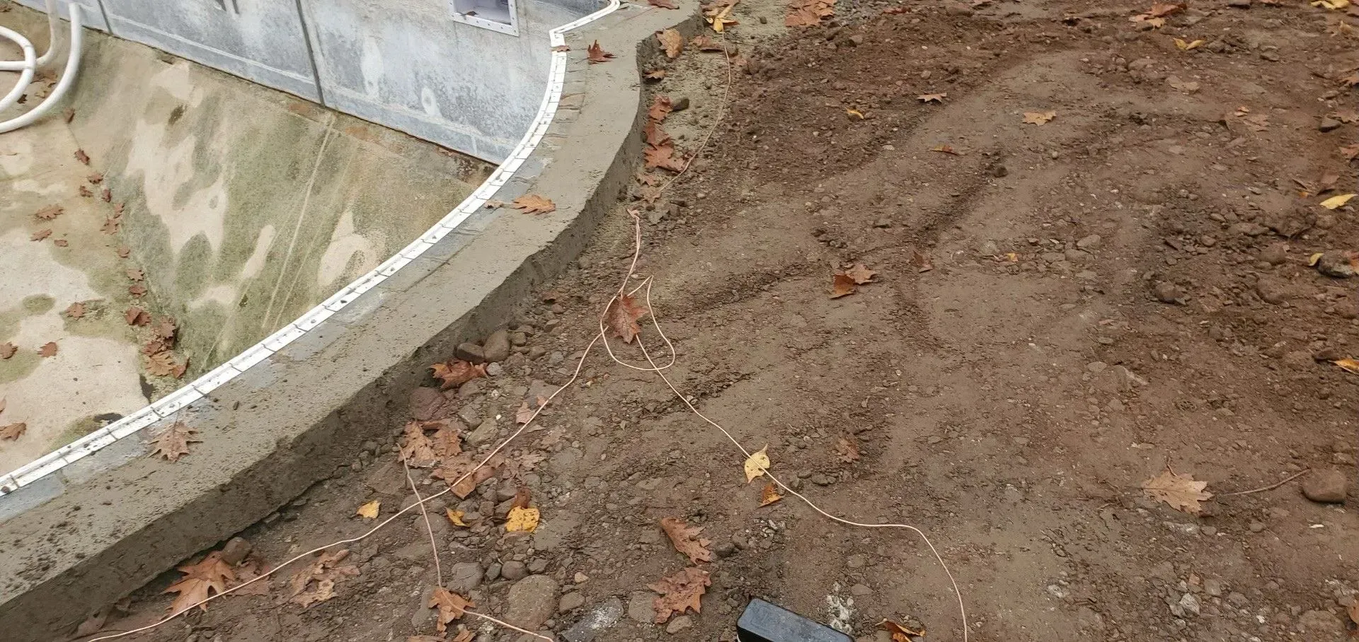 A concrete pool surrounded by dirt and leaves is being built.