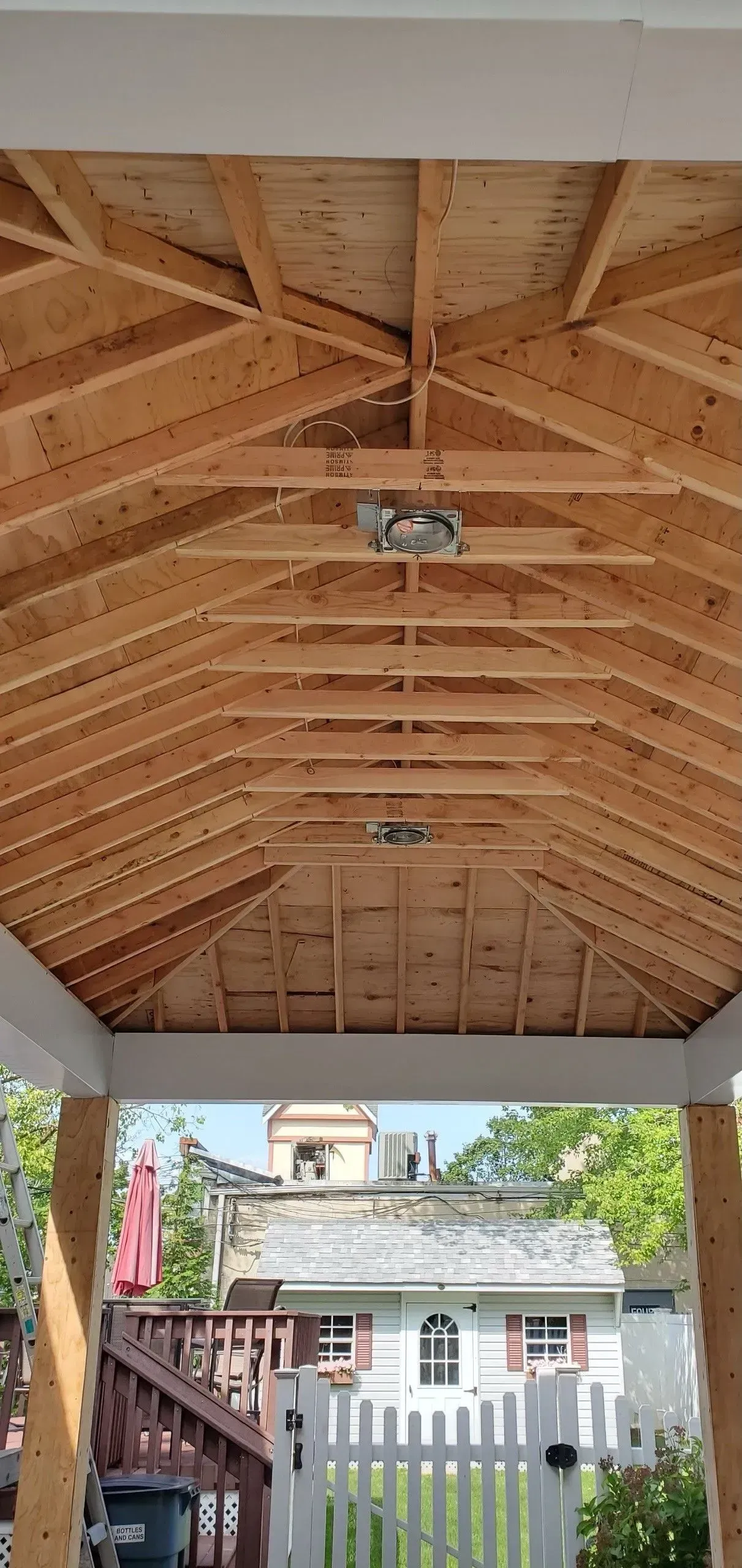 The ceiling of a wooden gazebo with a white fence in the background.