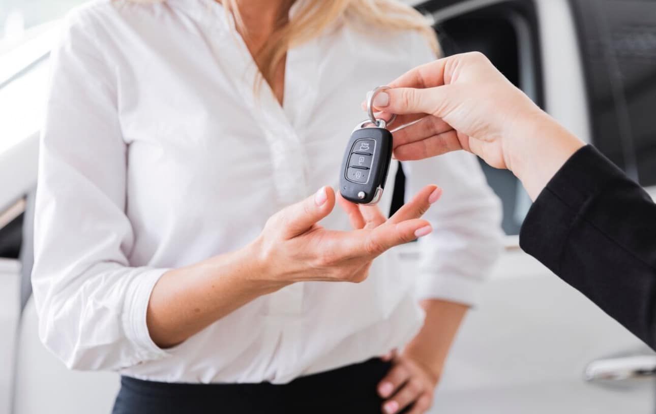 A woman is getting a car key from a car dealer.