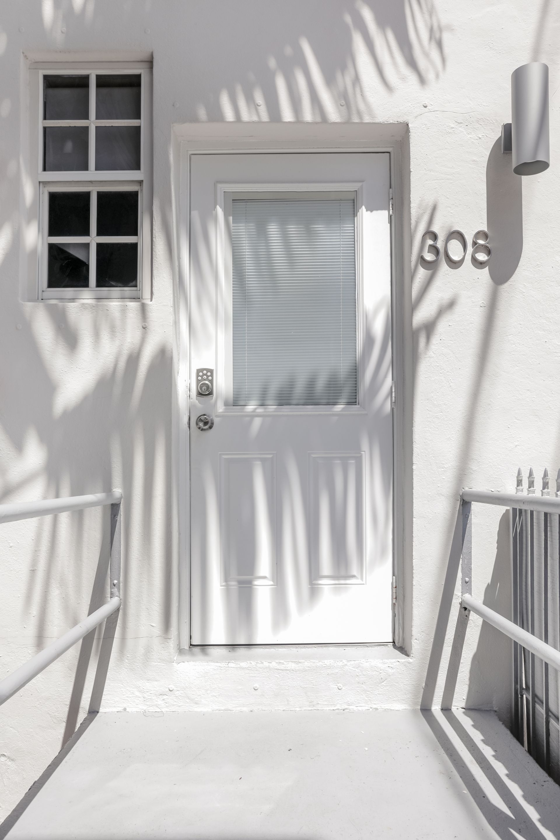White front door with glass panel and house number 608 beside a window and railings in bright sunlight