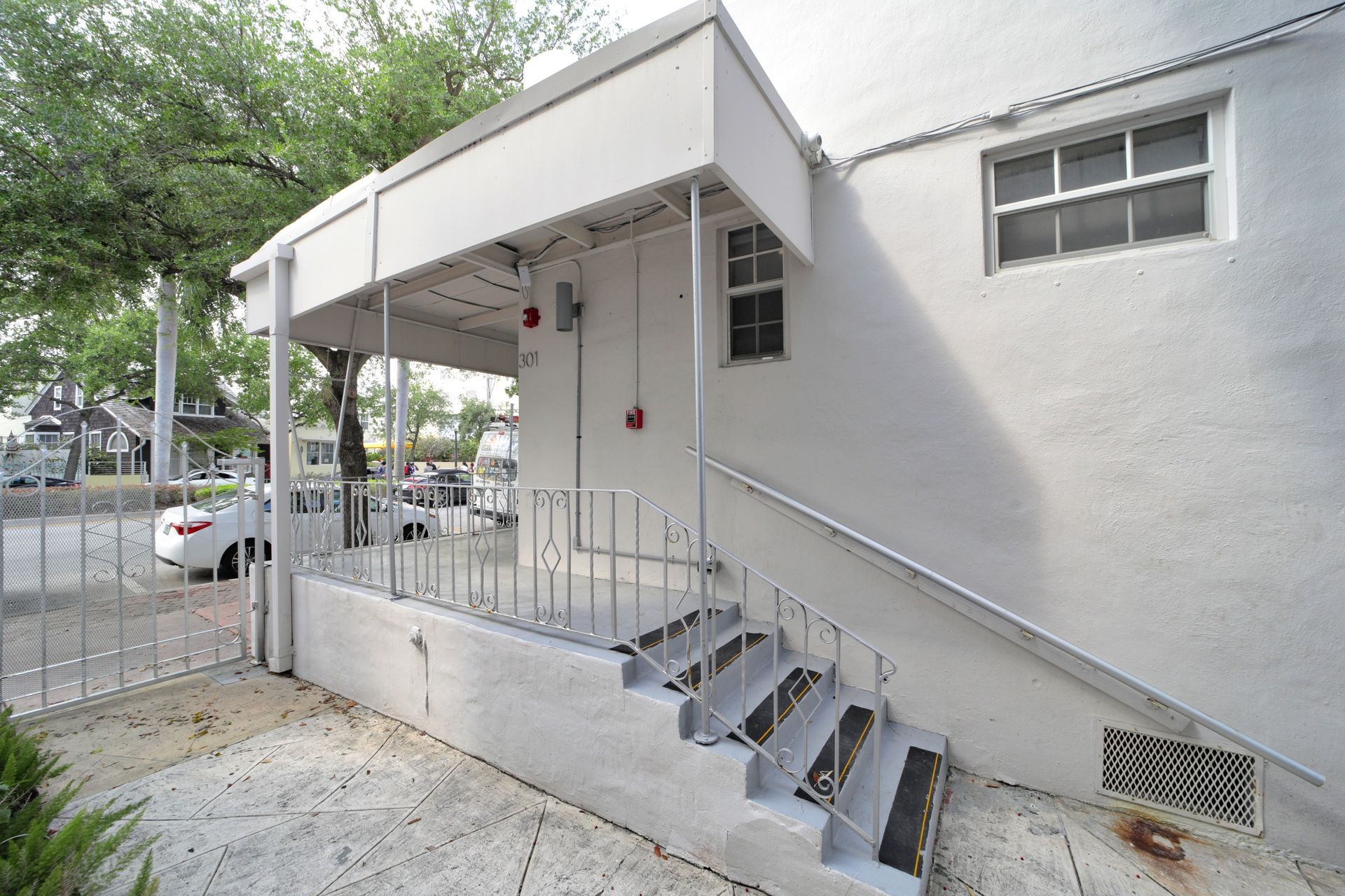 Exterior side entrance with white stairs, metal railing, and a covered porch on a white building.
