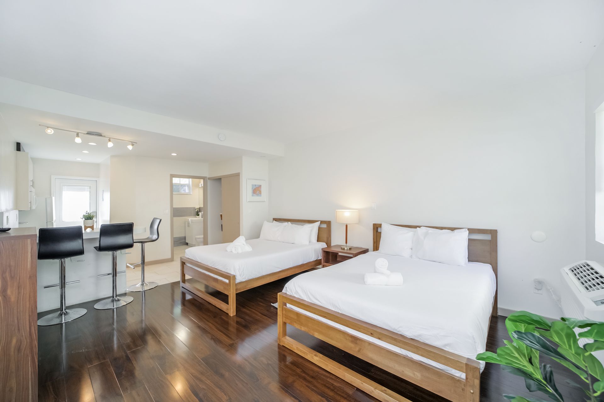 Bright hotel room with two wooden beds, dark wood floor, and a small bar seating area