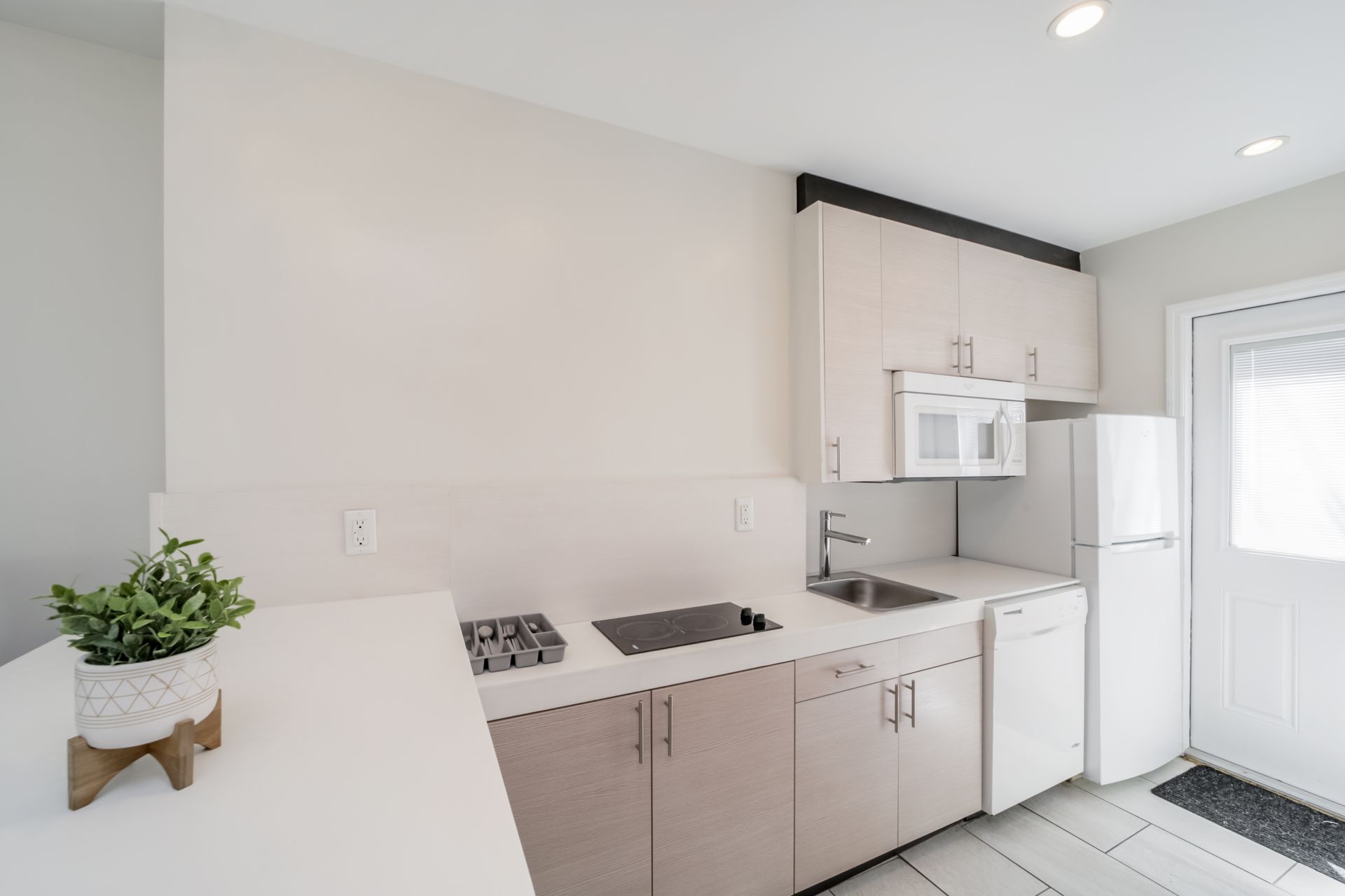Bright white kitchen with beige cabinets, white appliances, and a door to the outside.
