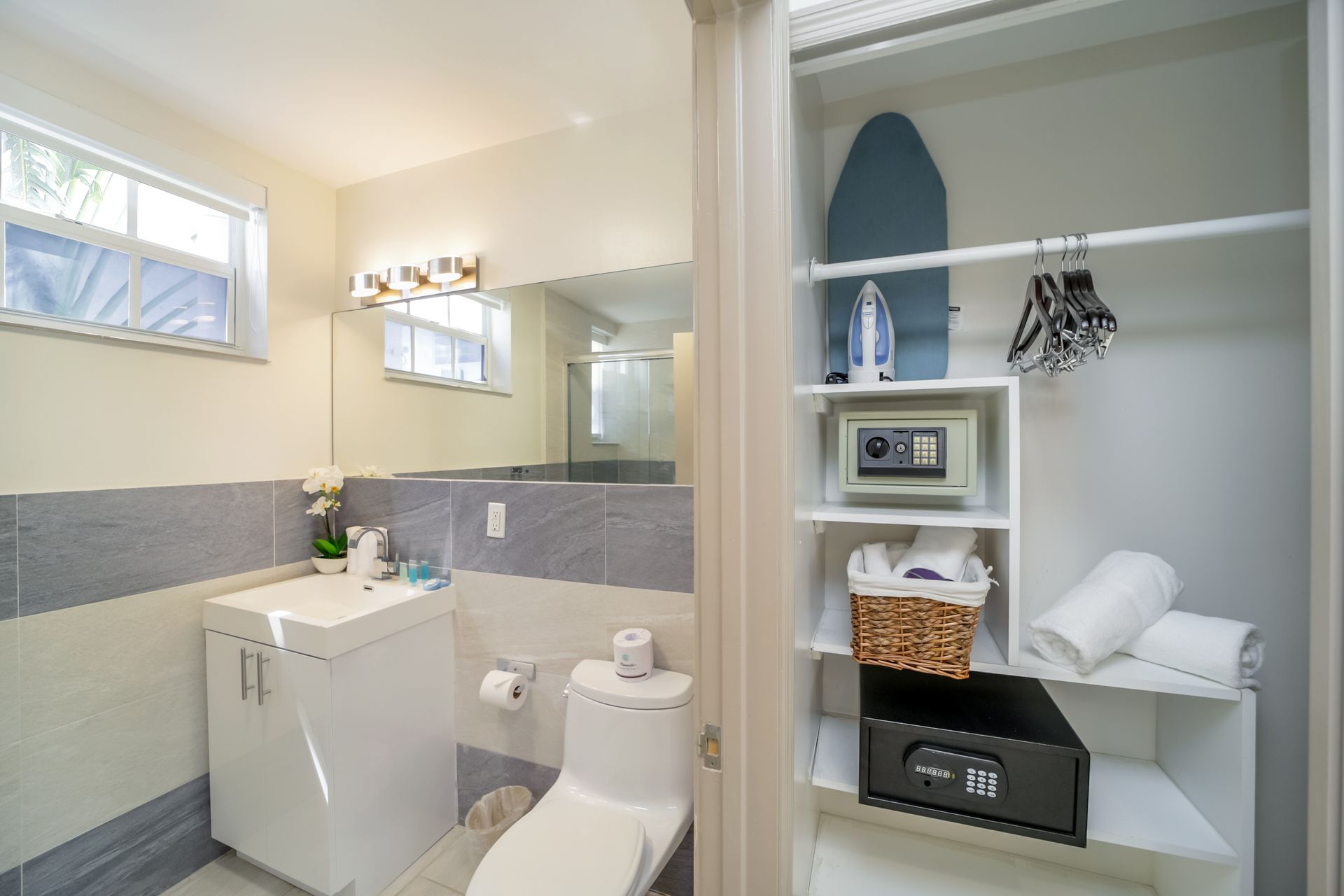 Bright white bathroom with vanity, toilet, mirror, and open shelving with towels and decor
