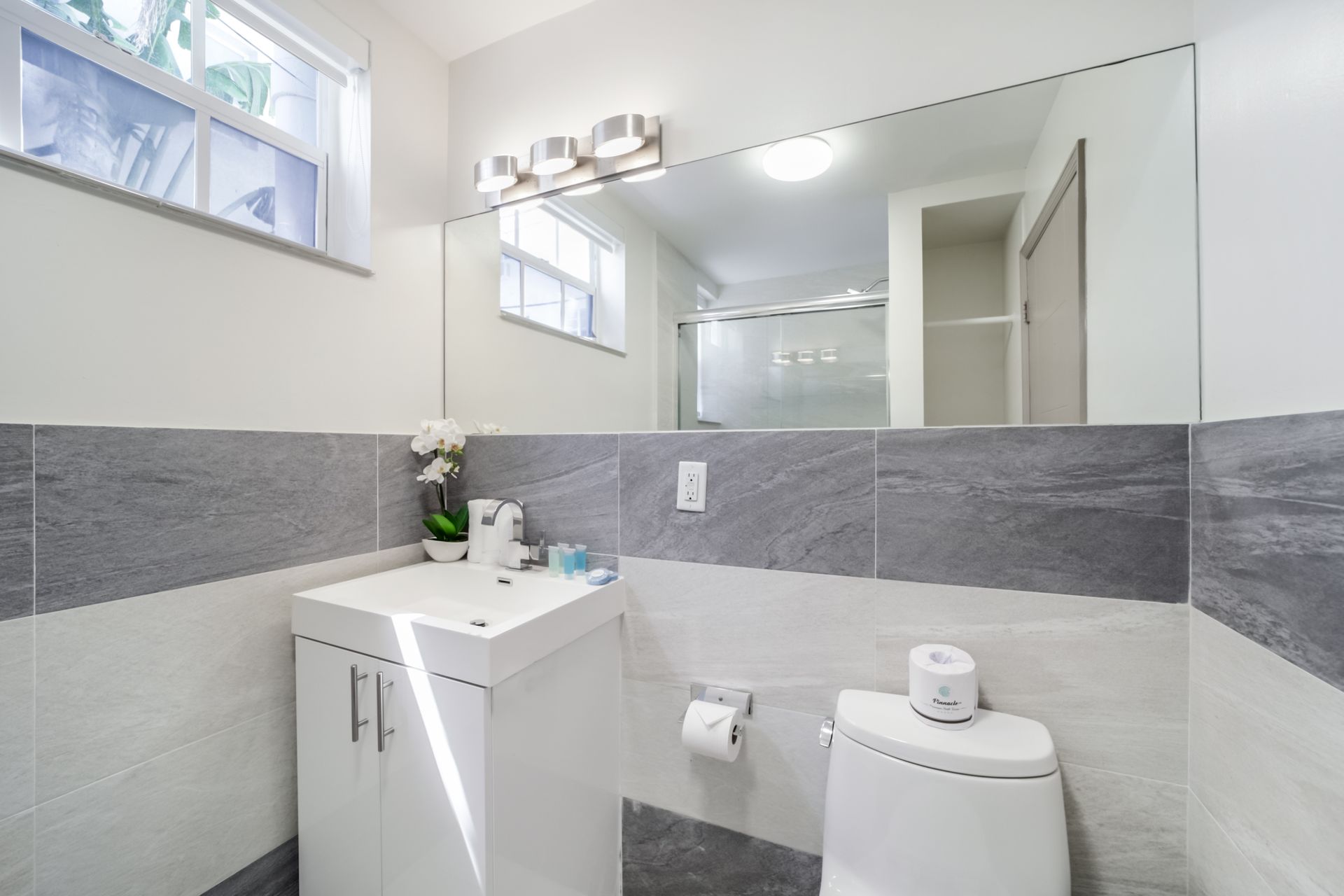 Modern bathroom with white vanity, large mirror, gray tile accents, and a toilet.