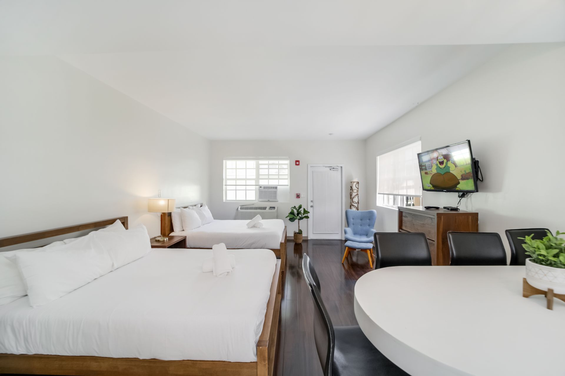 Bright attic studio with a bed, sofa, desk, wall TV, and round dining table; white walls and dark wood floor