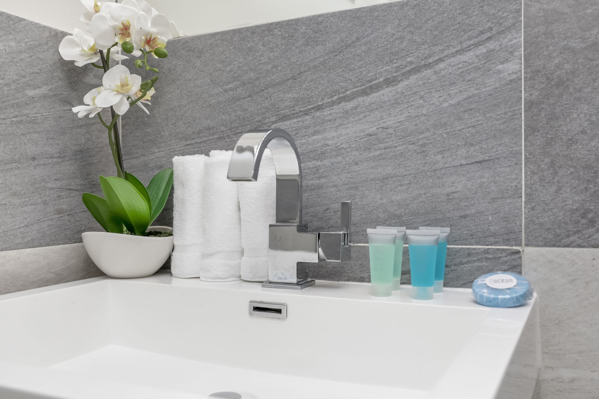 Modern bathroom sink with chrome faucet, white towels, orchid, and blue toiletries on a white vanity