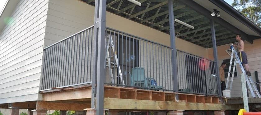 A man is standing on a ladder on the porch of a house.