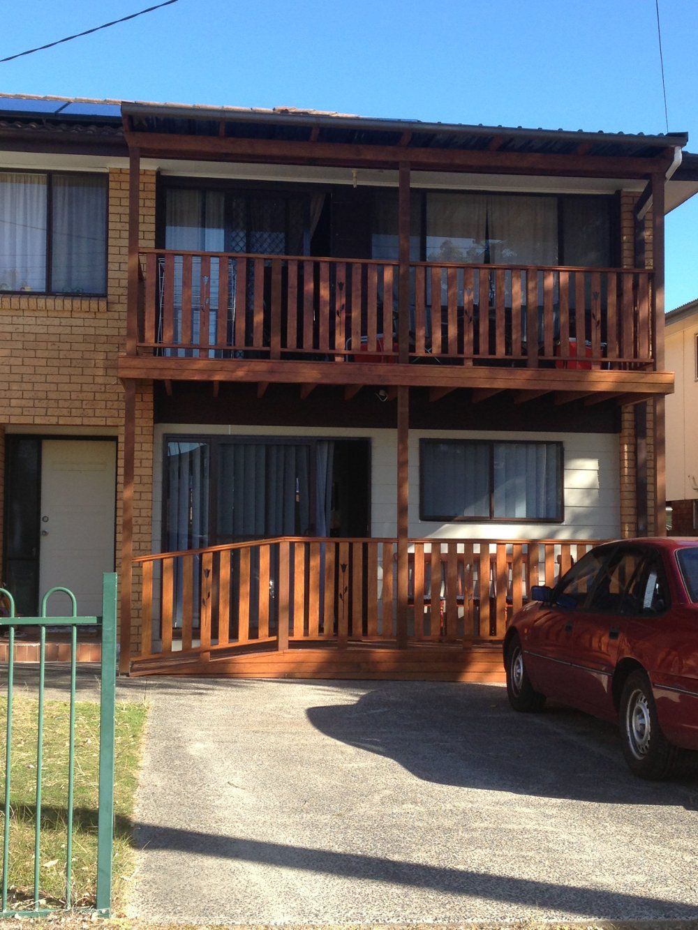 A red car is parked in front of a house with a balcony