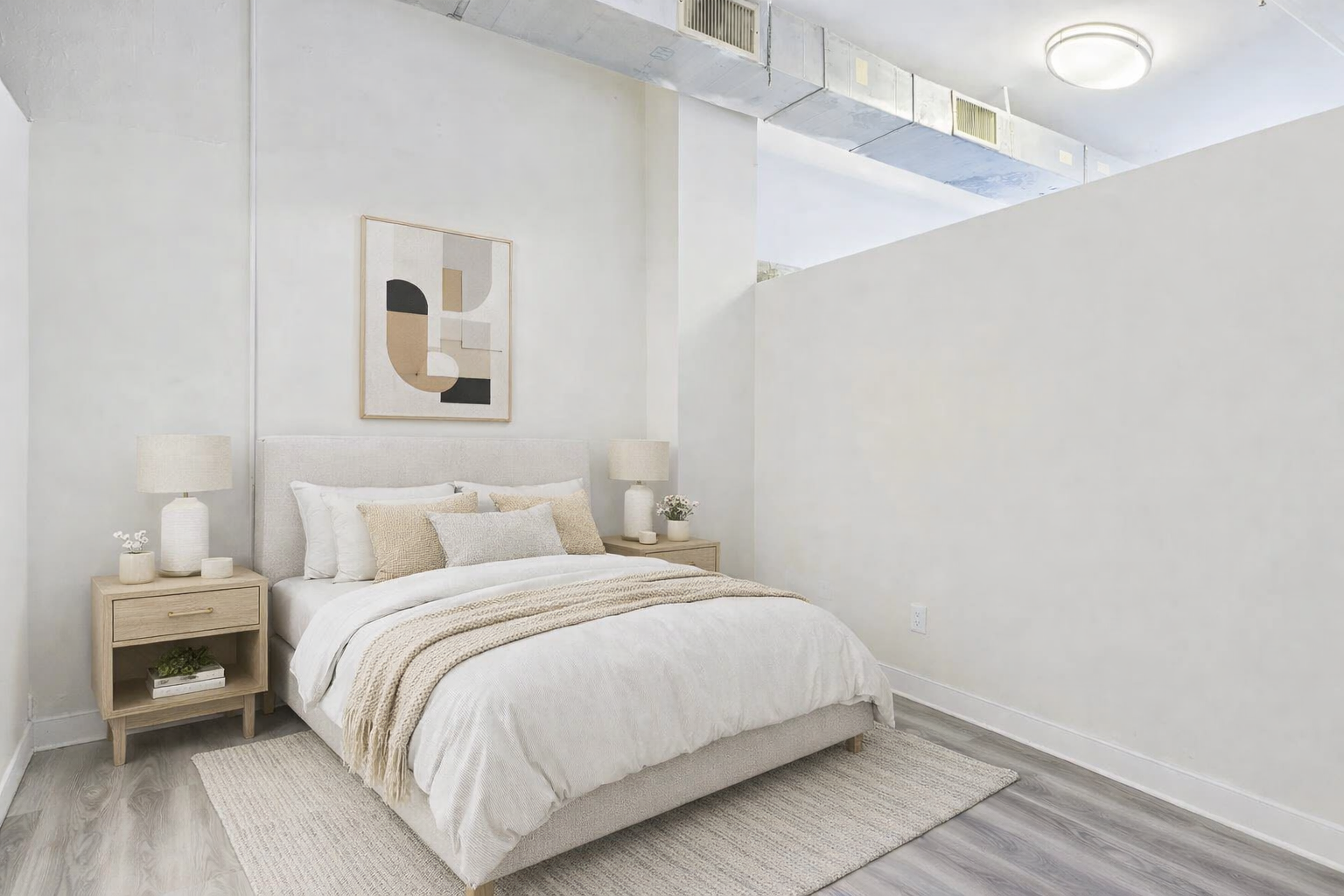 Bedroom with a bed, nightstands, rug, and artwork. White walls and neutral decor.