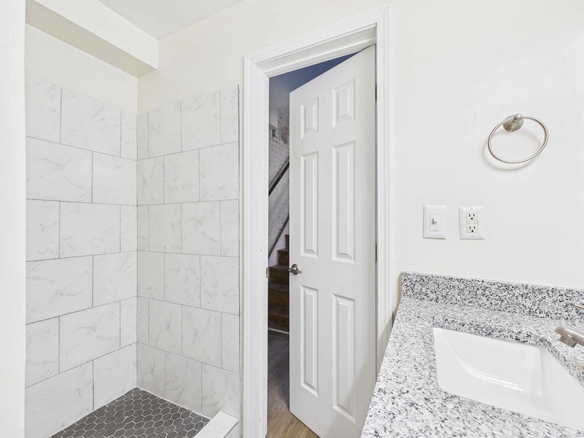 Bathroom with tiled shower, vanity, and open door leading to stairs.