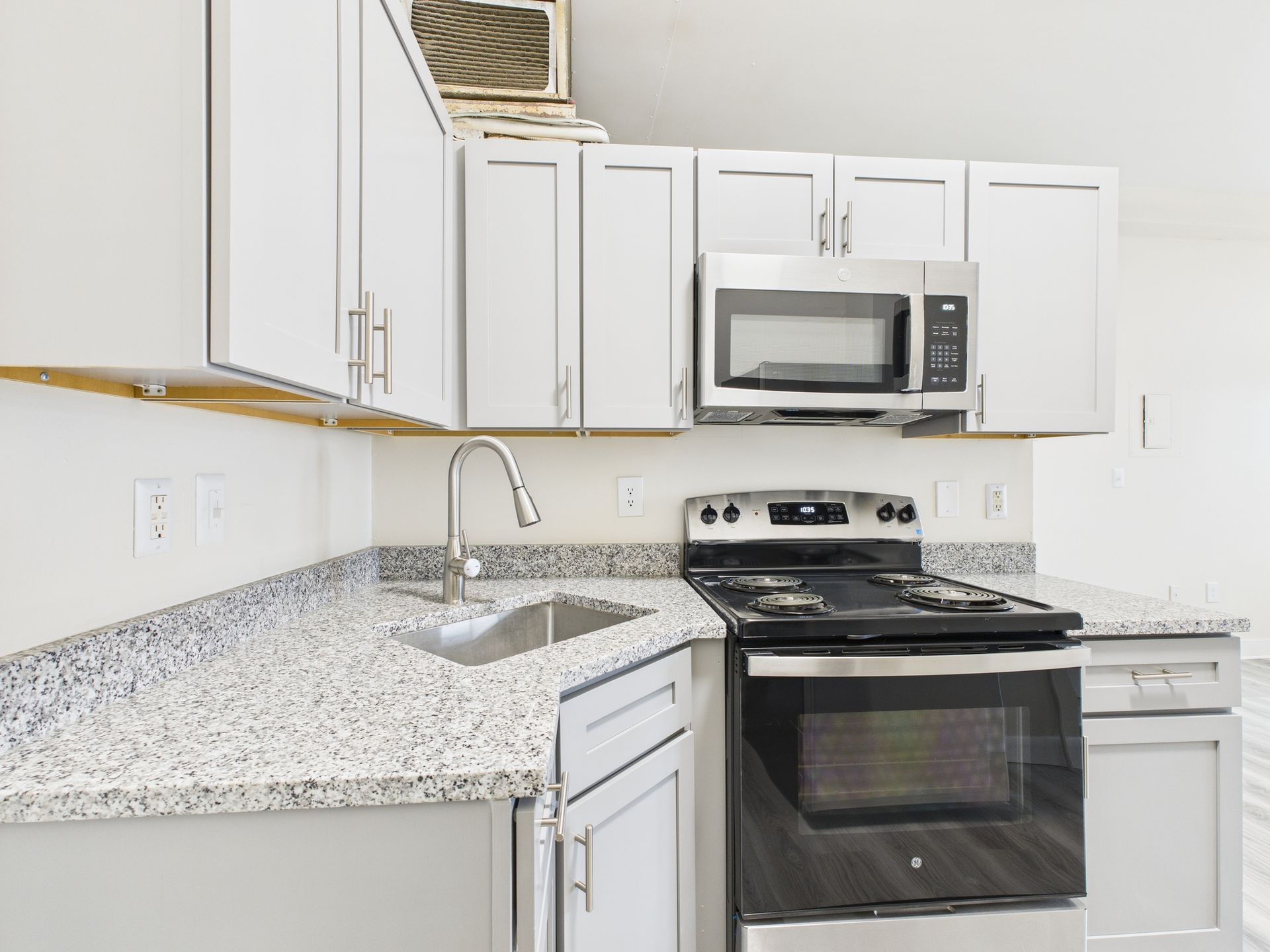 A small kitchen with light gray cabinets, speckled countertop, and stainless steel appliances.