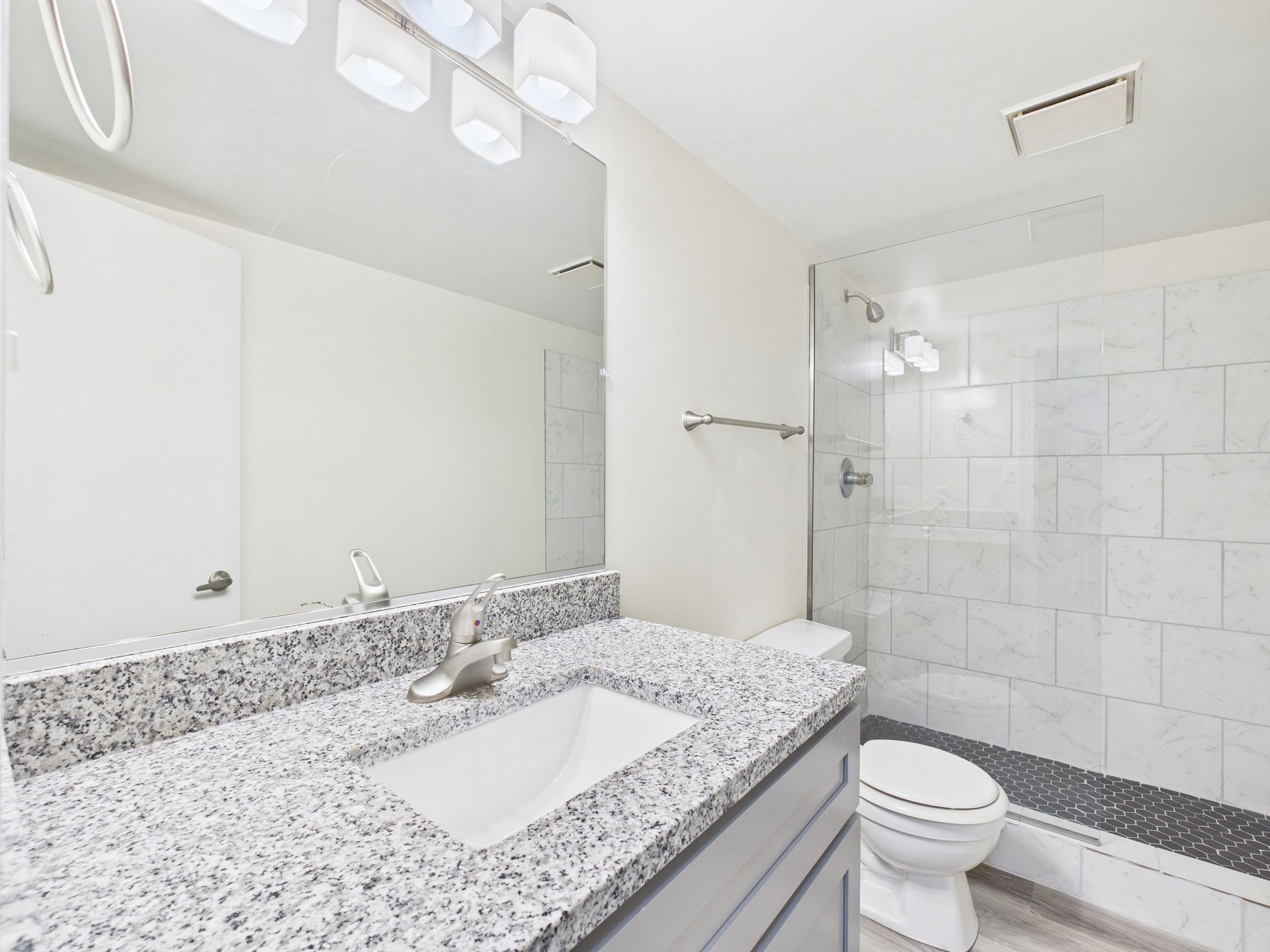 Bathroom with granite countertop, large mirror, white toilet, and tiled shower.