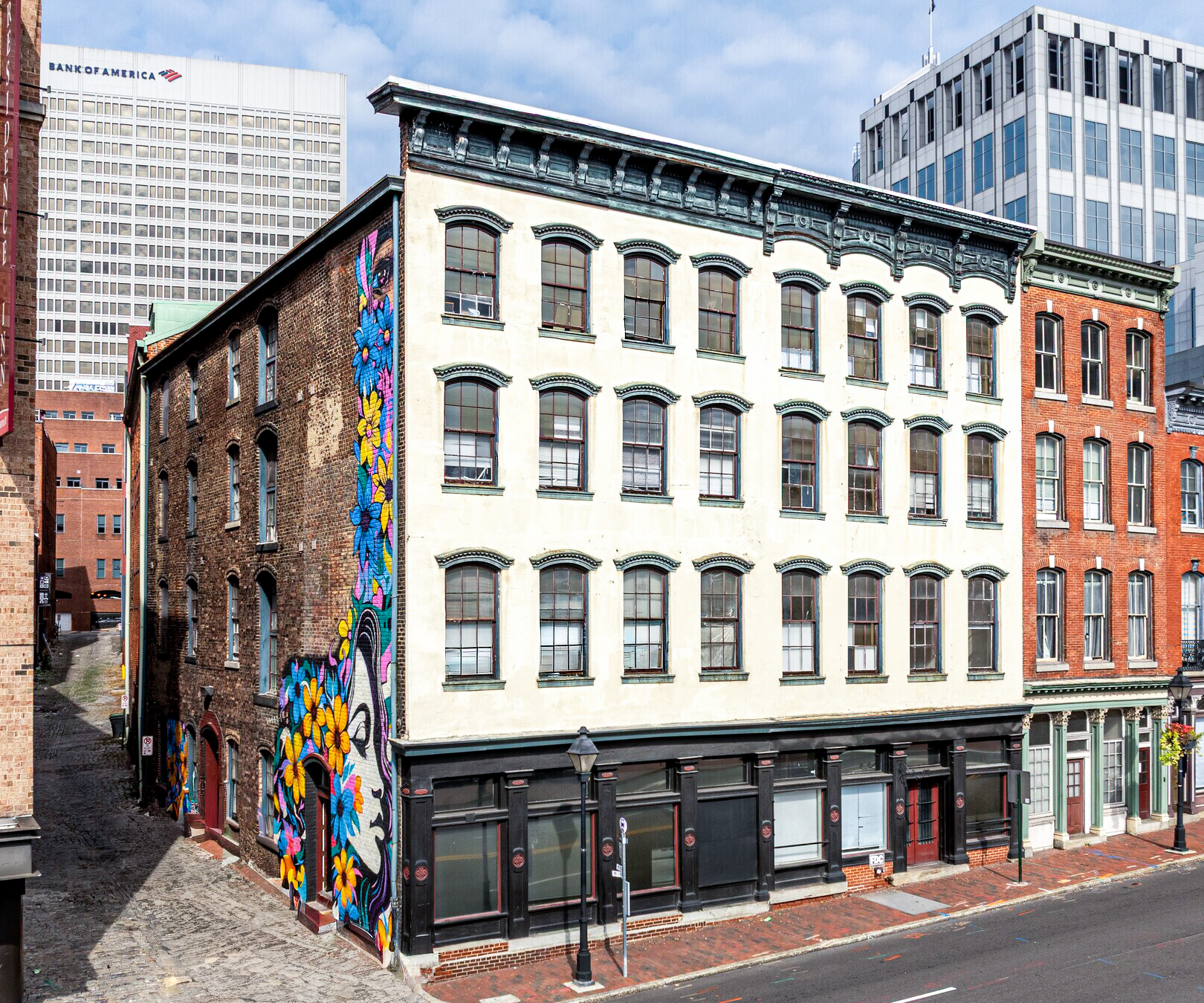 Historic multi-story building with mural and shops, in a city with brick and modern buildings.
